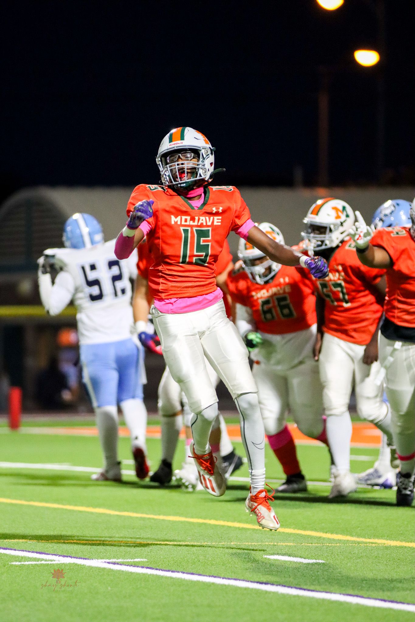 Football player in orange jersey leaping on field during nighttime game.