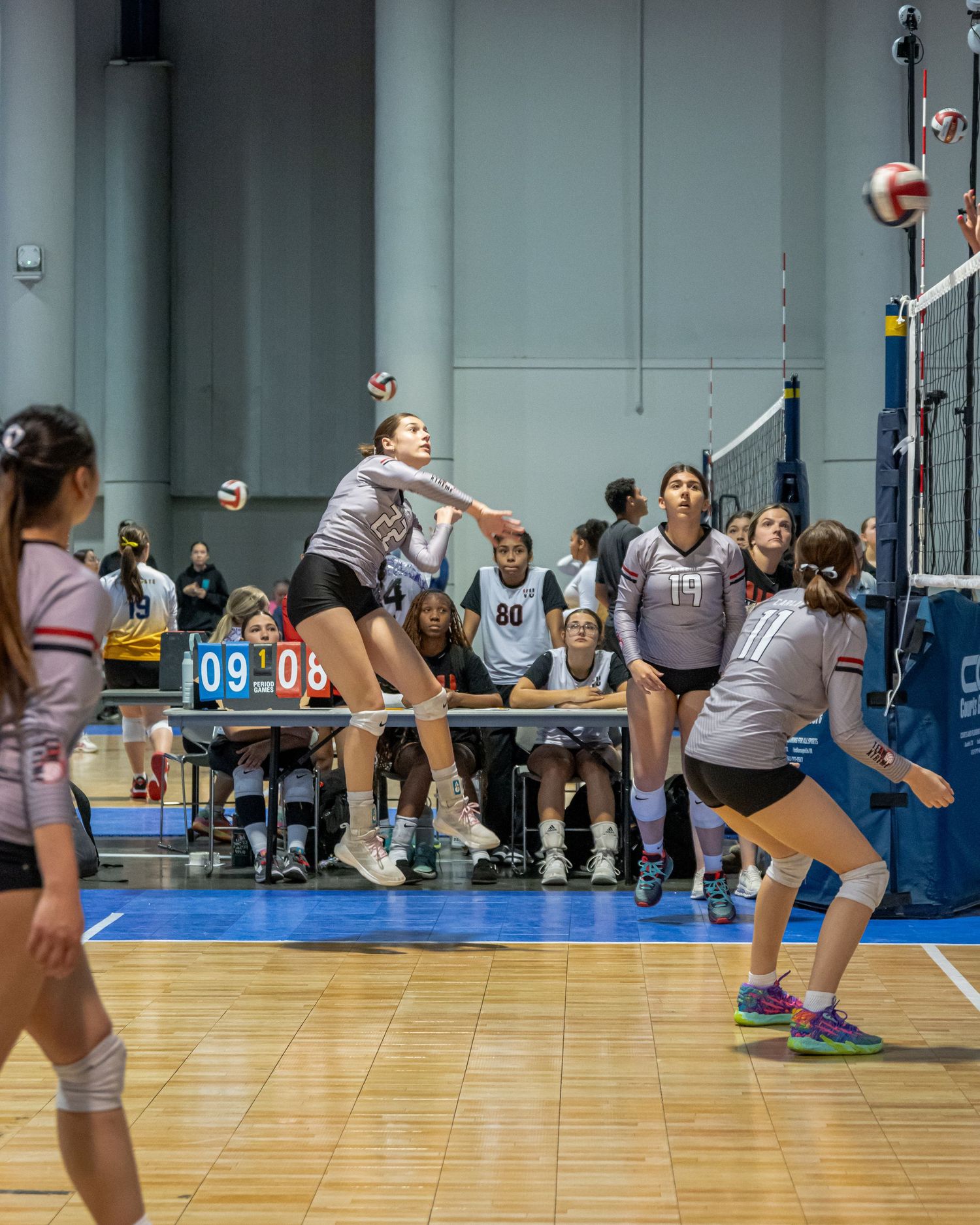 Indoor volleyball players compete in a dynamic game with players diving and jumping for the ball.