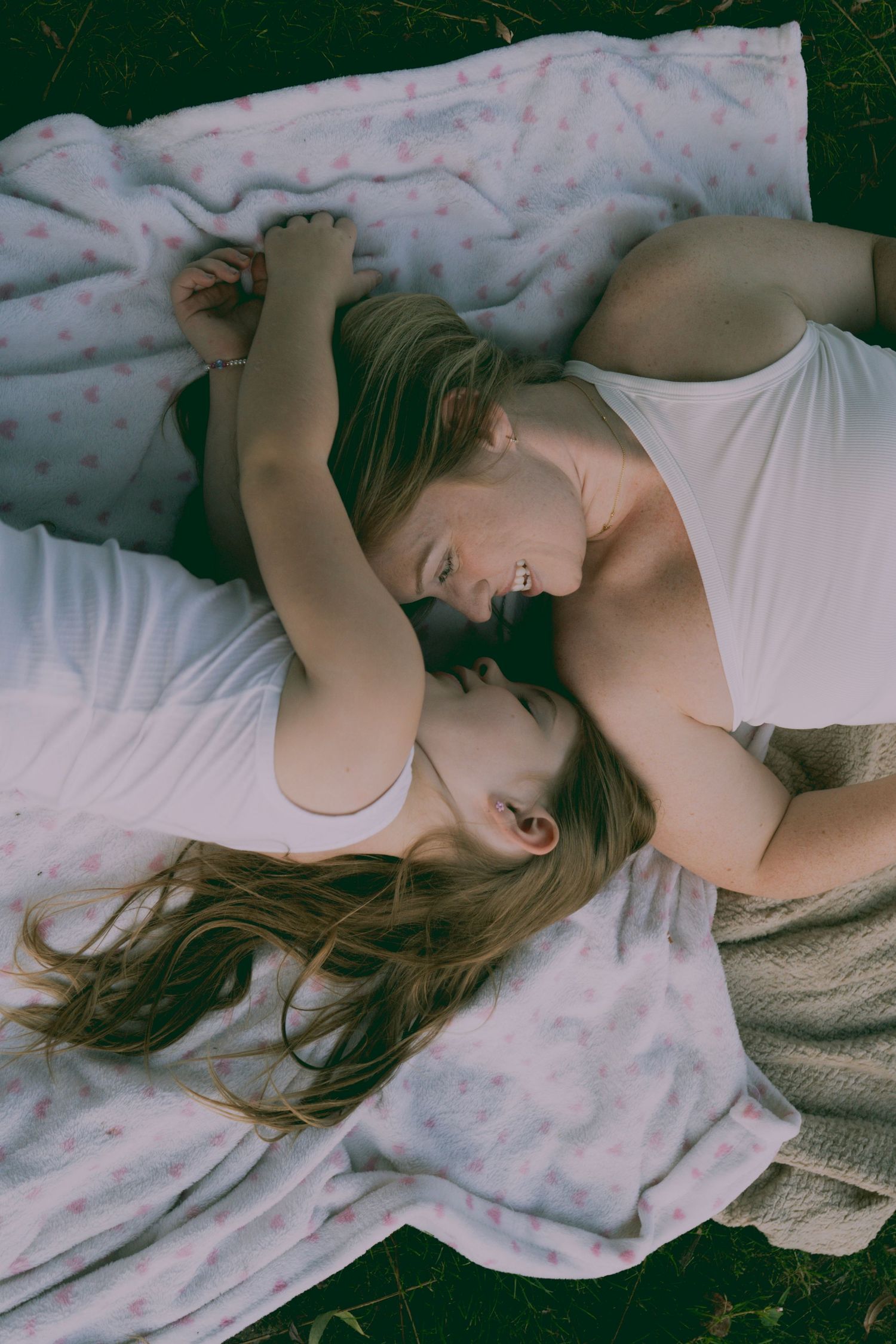 A person in a white top lies down on white bedding and grass in a series of artistic portraits.