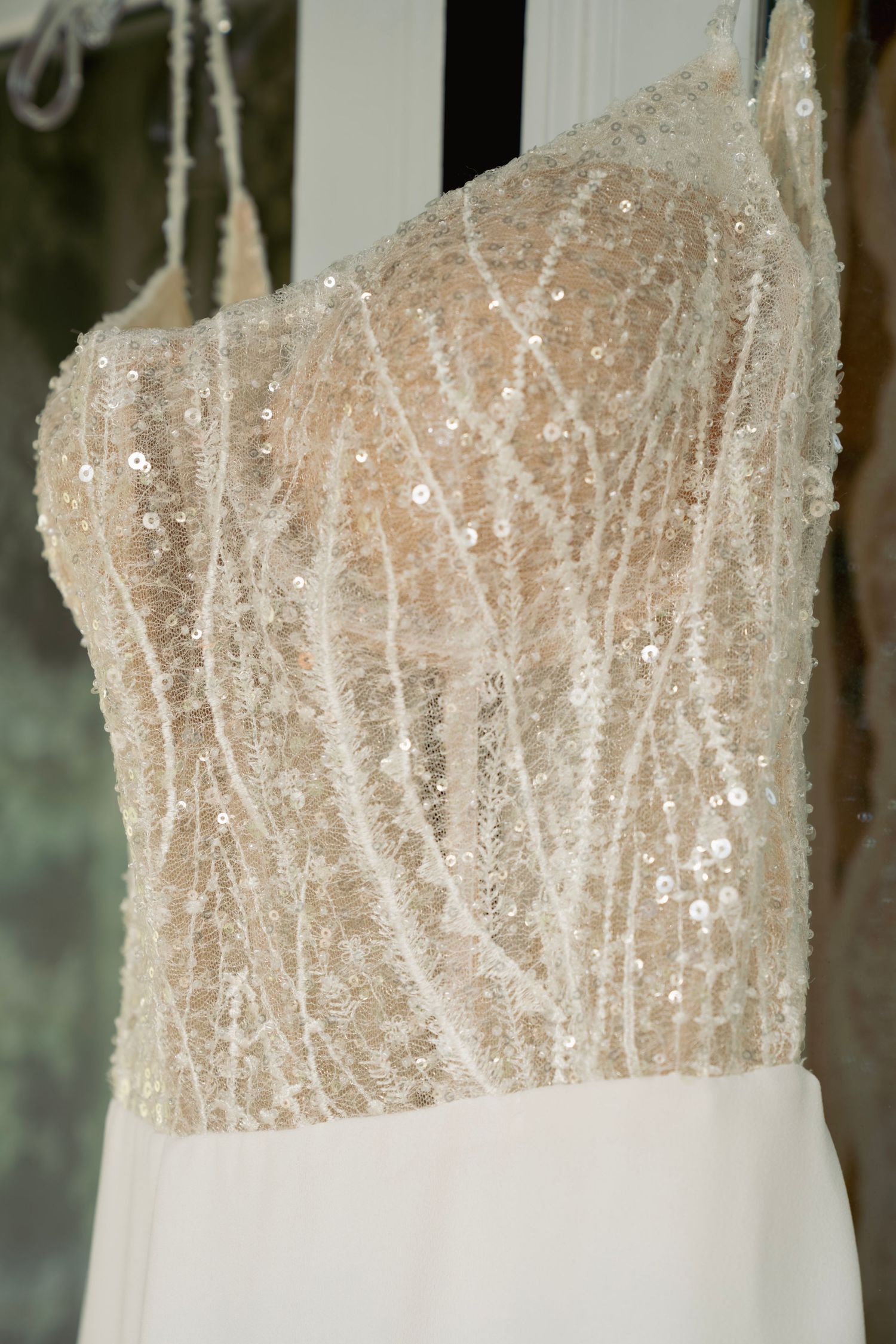 Three elegant white wedding dresses with intricate beaded bodices displayed on hangers against a neutral background.