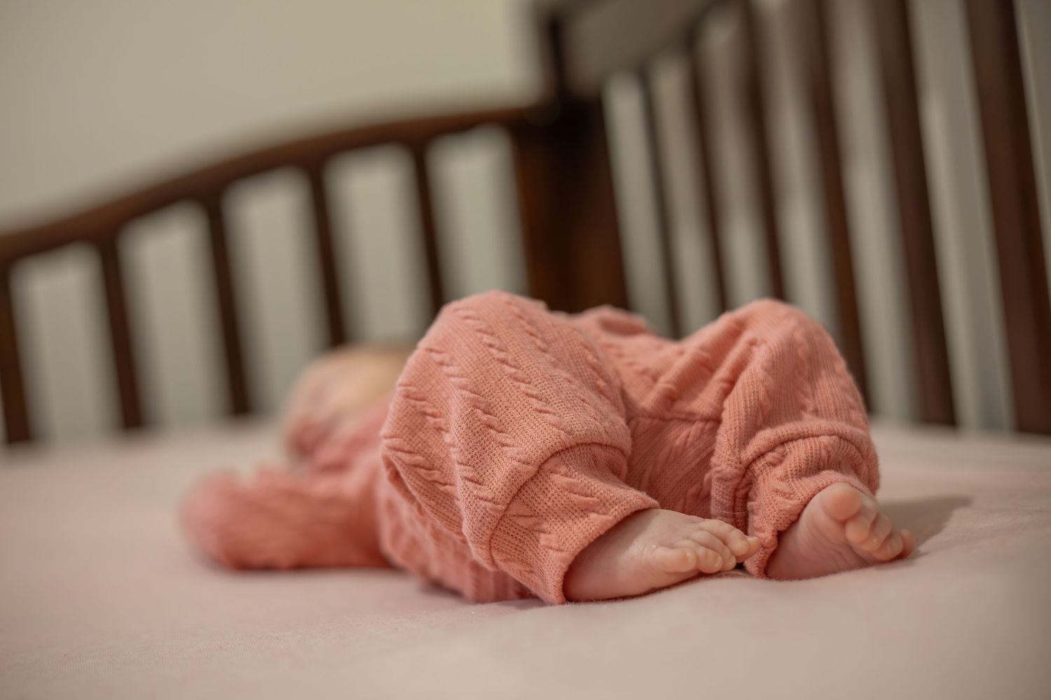 A collection of photos showing a sleeping baby swaddled in pink blankets on a wooden crib.