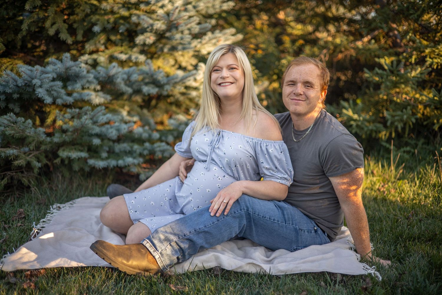 A couple relaxing on a blanket during an outdoor maternity photoshoot.