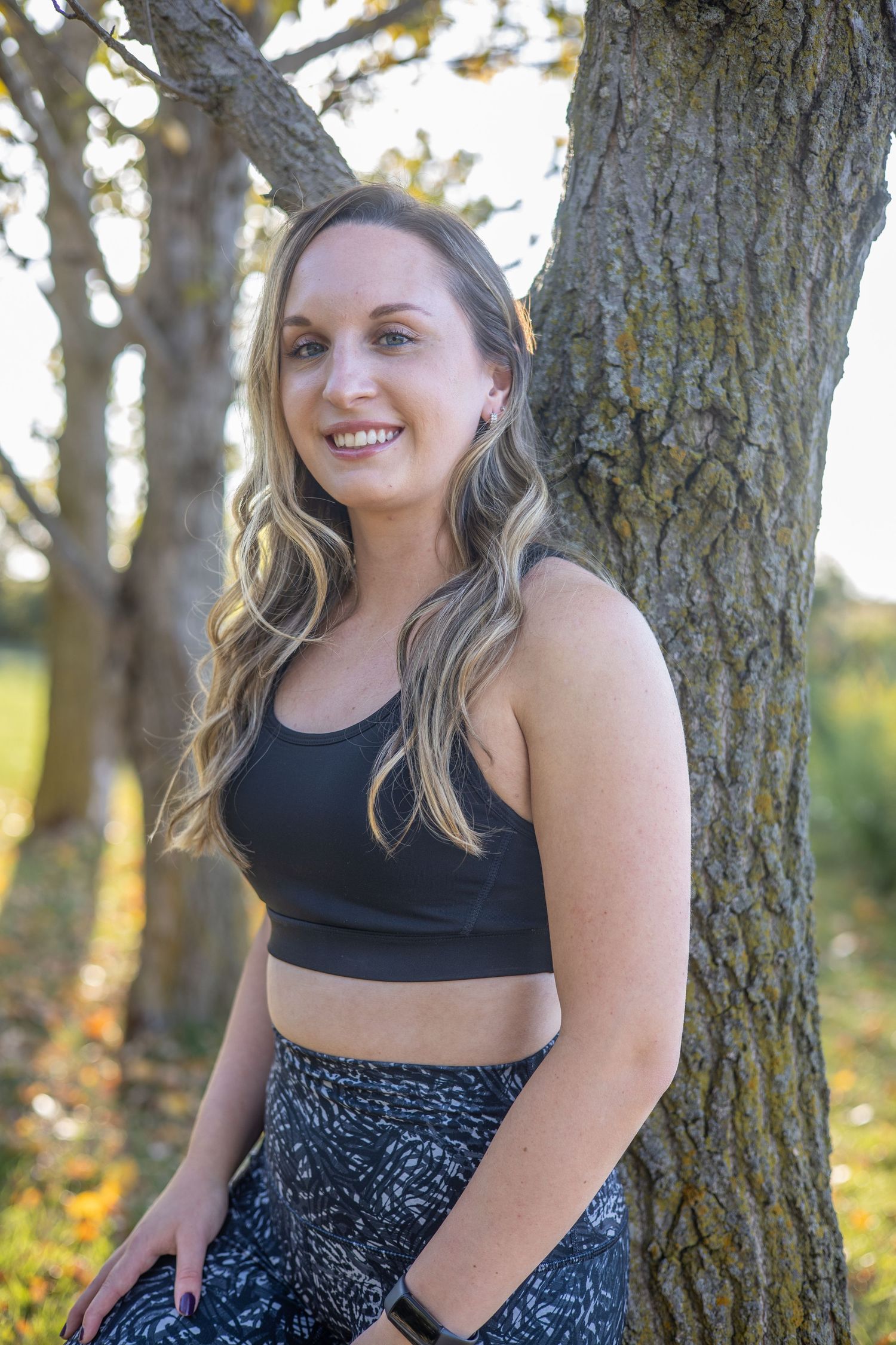 Person in athletic wear sitting against tree trunk in golden sunlight.