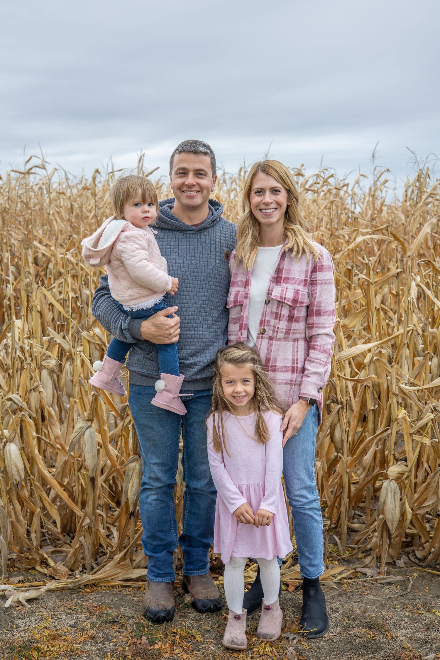 Family poses together in front of tall dried corn stalks during autumn photo session. During Family session