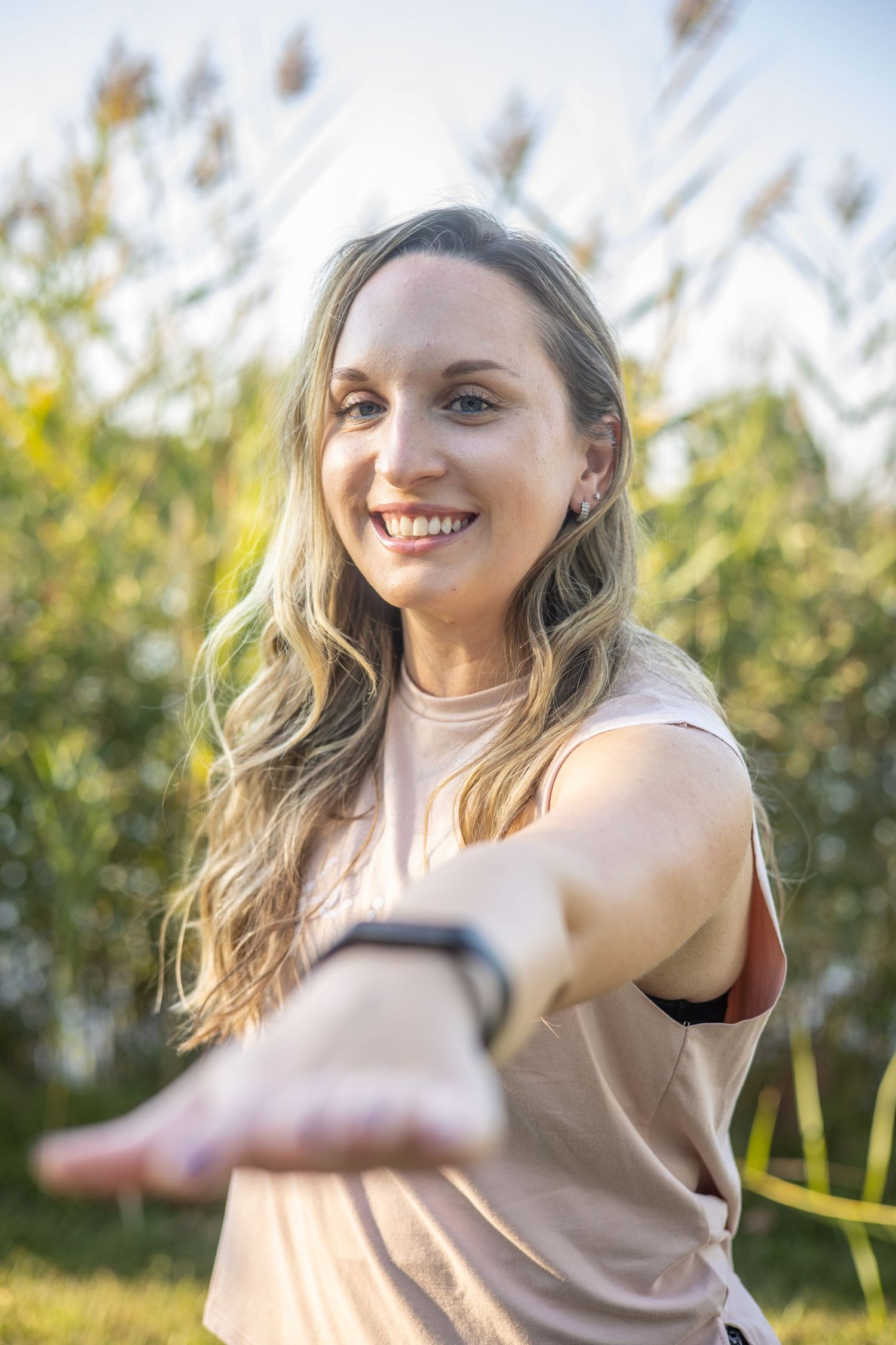 A golden hour portrait of someone reaching toward the camera with tall grass in background. During a Portrait session