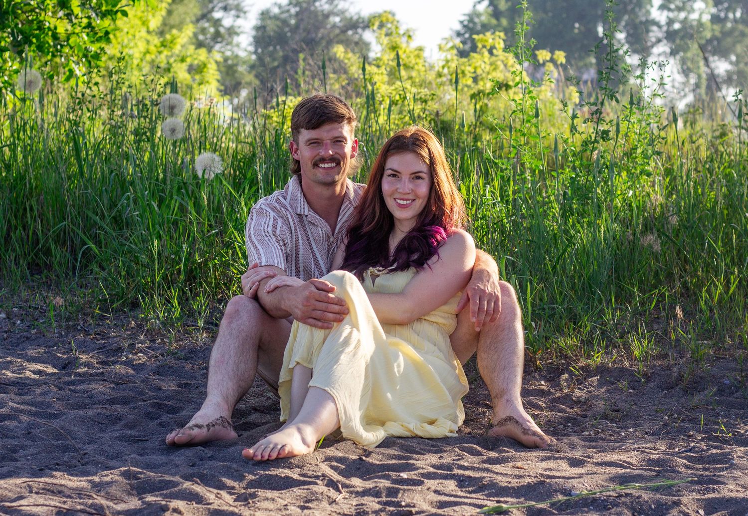 People sit together on a beach with lush greenery in the background.