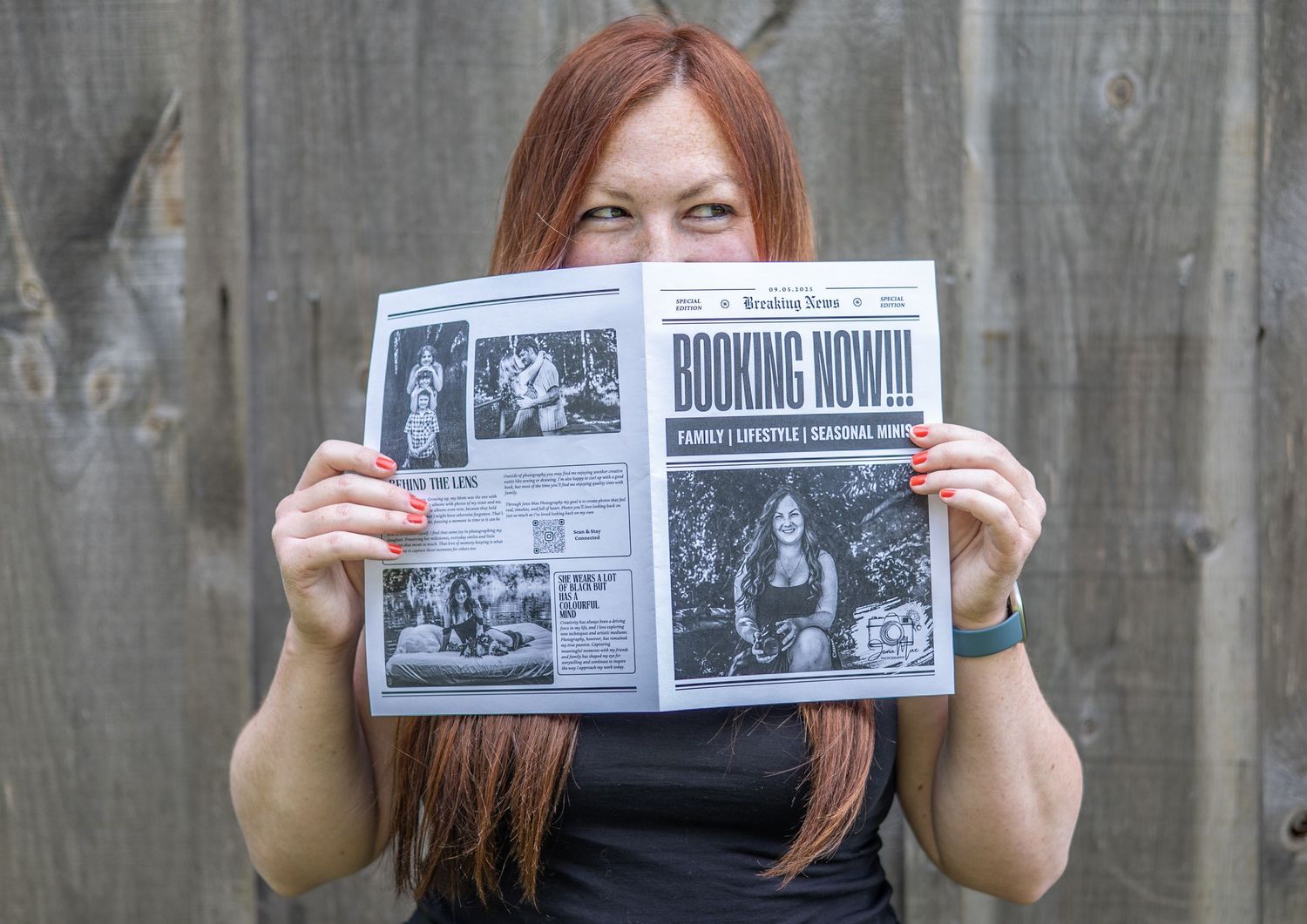 Person holding up vintage-style newspaper pages against concrete wall.