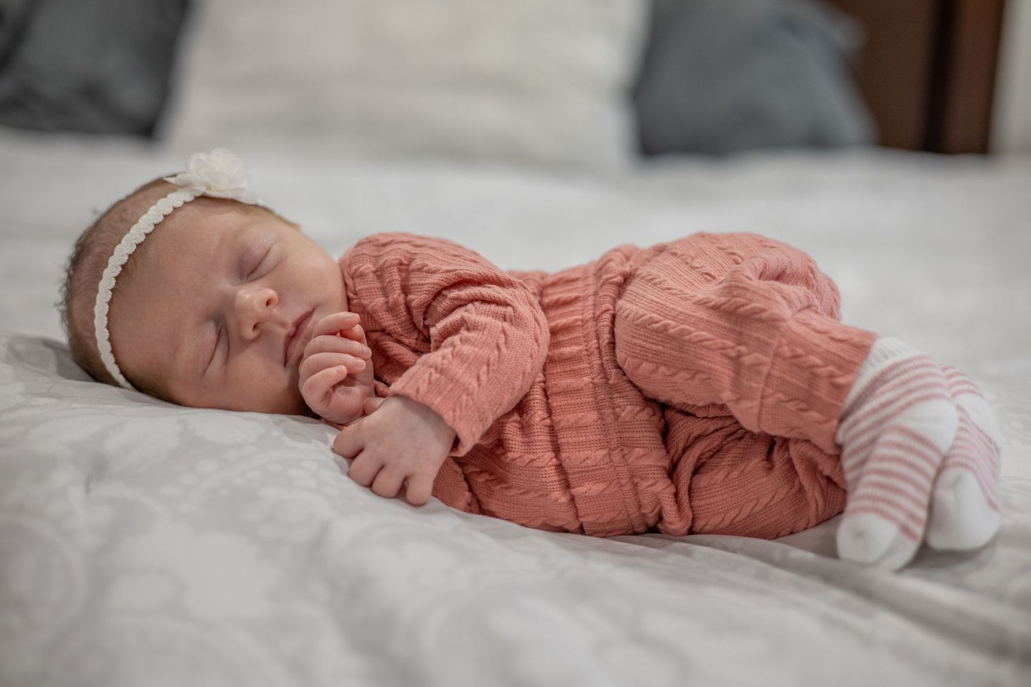 A sleeping baby wearing a coral-colored outfit lies peacefully on white bedding.