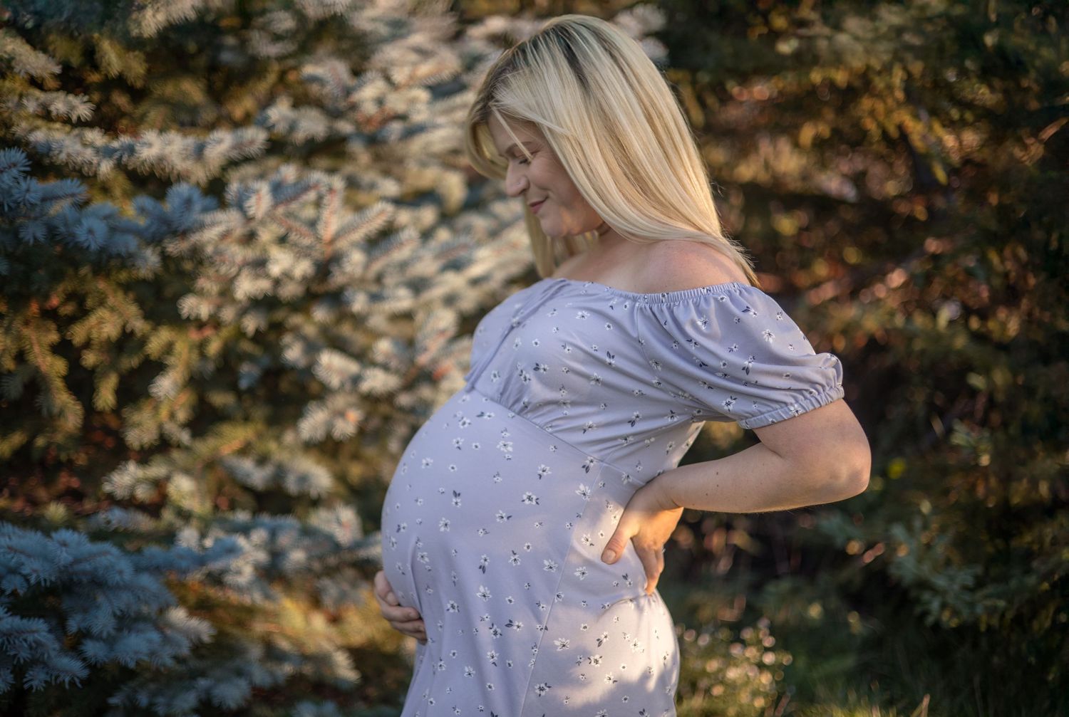 Side view of a pregnant woman in a polka dot dress backlit by sunset.