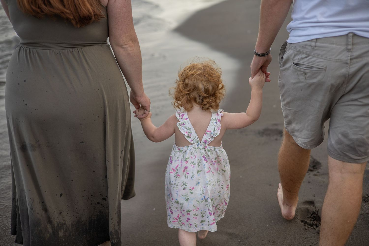 Family walking together on sandy beach holding hands during sunset.