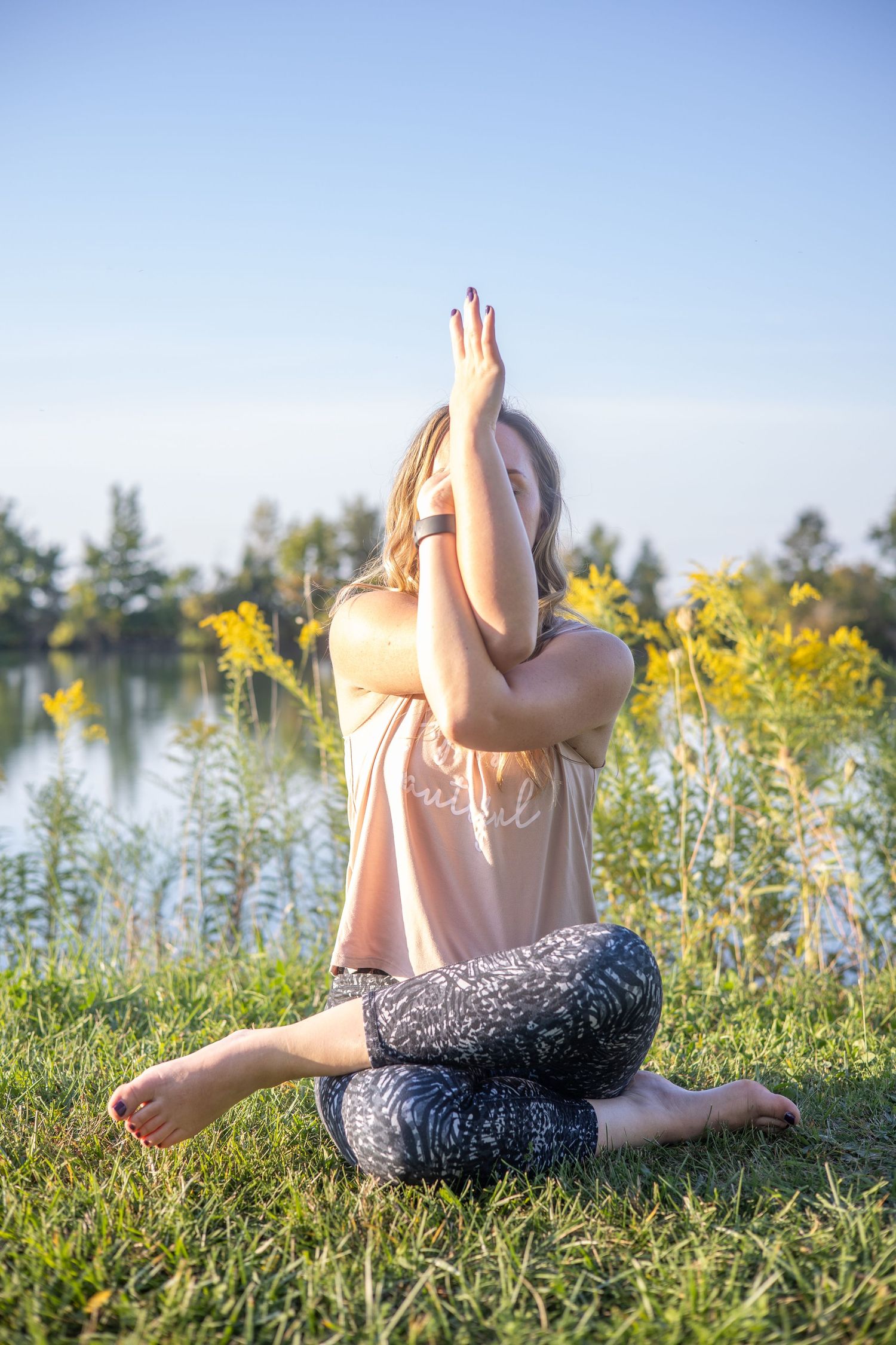 Person relaxing in field of yellow wildflowers beside lake on sunny day.