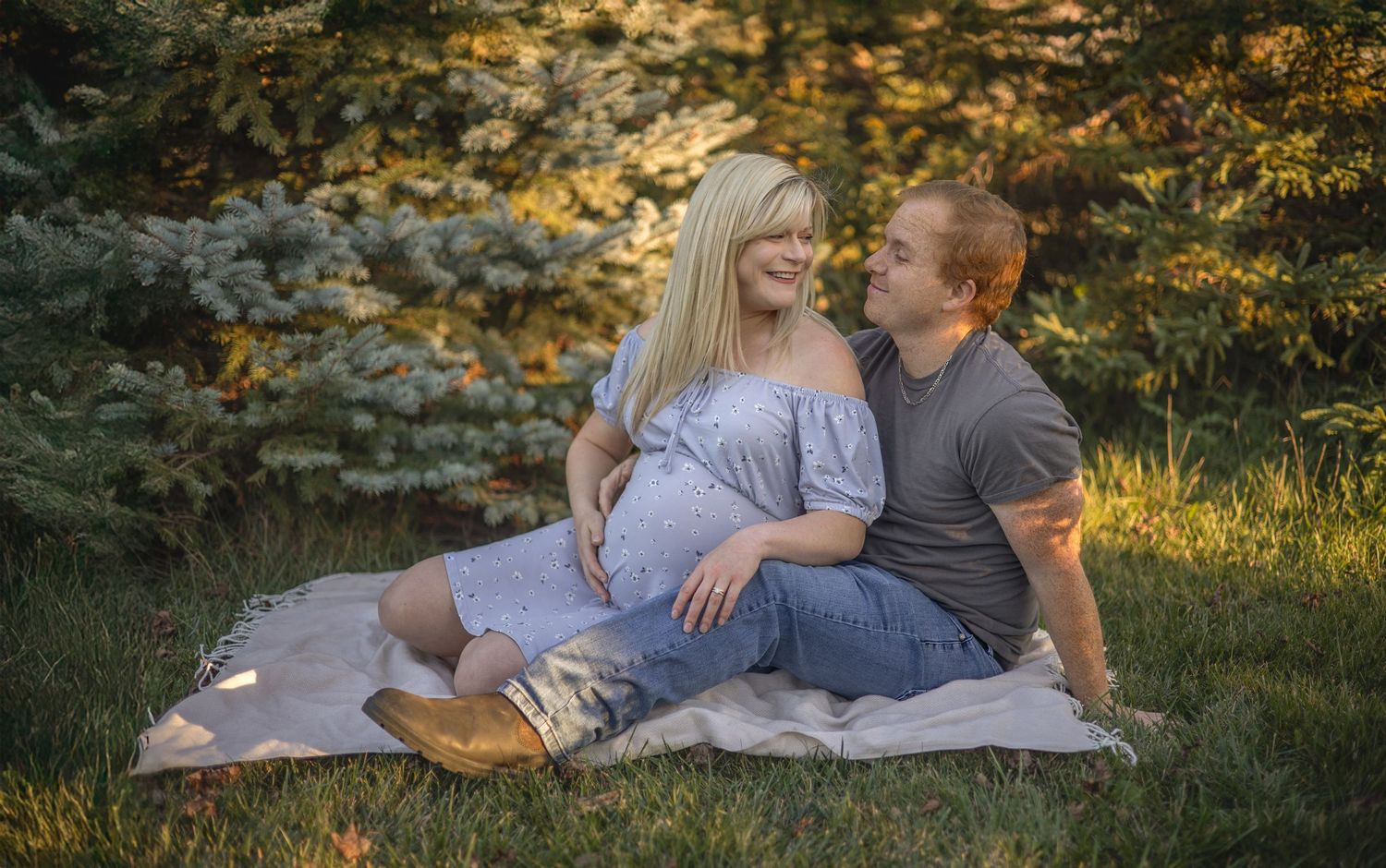 A couple sits on a blanket in a sunlit autumn garden setting, during maternity session