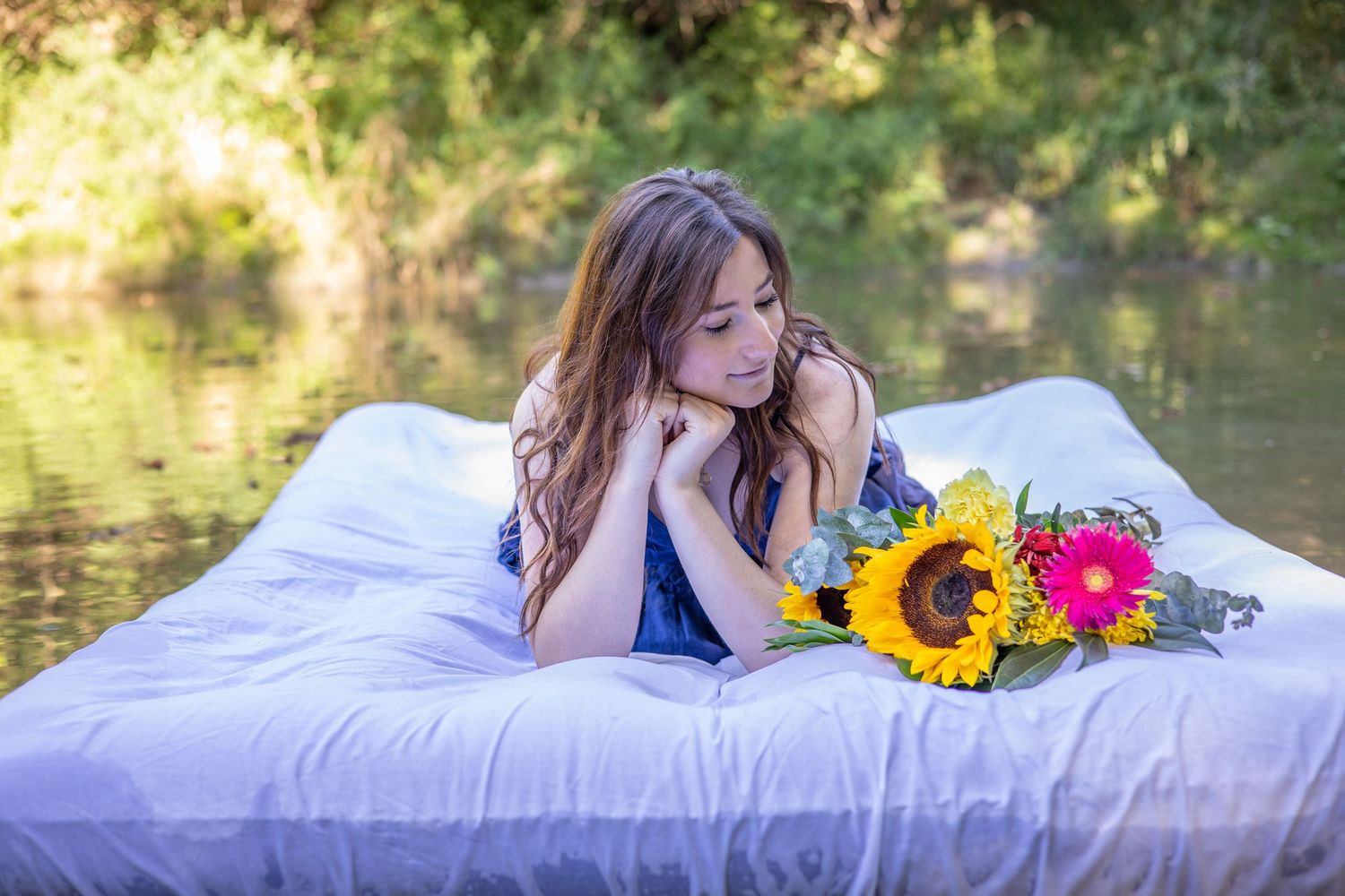 Dreamy outdoor photo with sunflowers and white bedding near a pond.