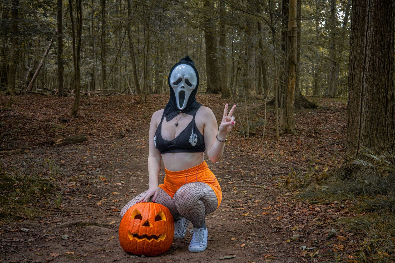 Halloween themed forest photoshoot with pumpkins and spooky masks on fallen leaves.
