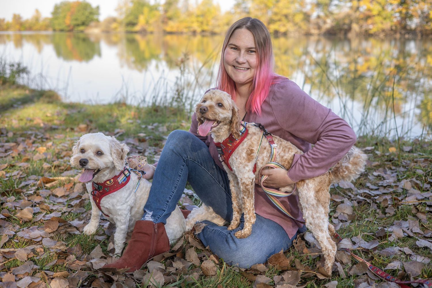 Two happy dogs posing with their owner by a scenic autumn lake. During Portrait Session