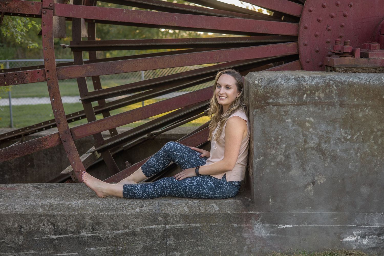 Person in workout attire posing near rustic metal bridge structure.