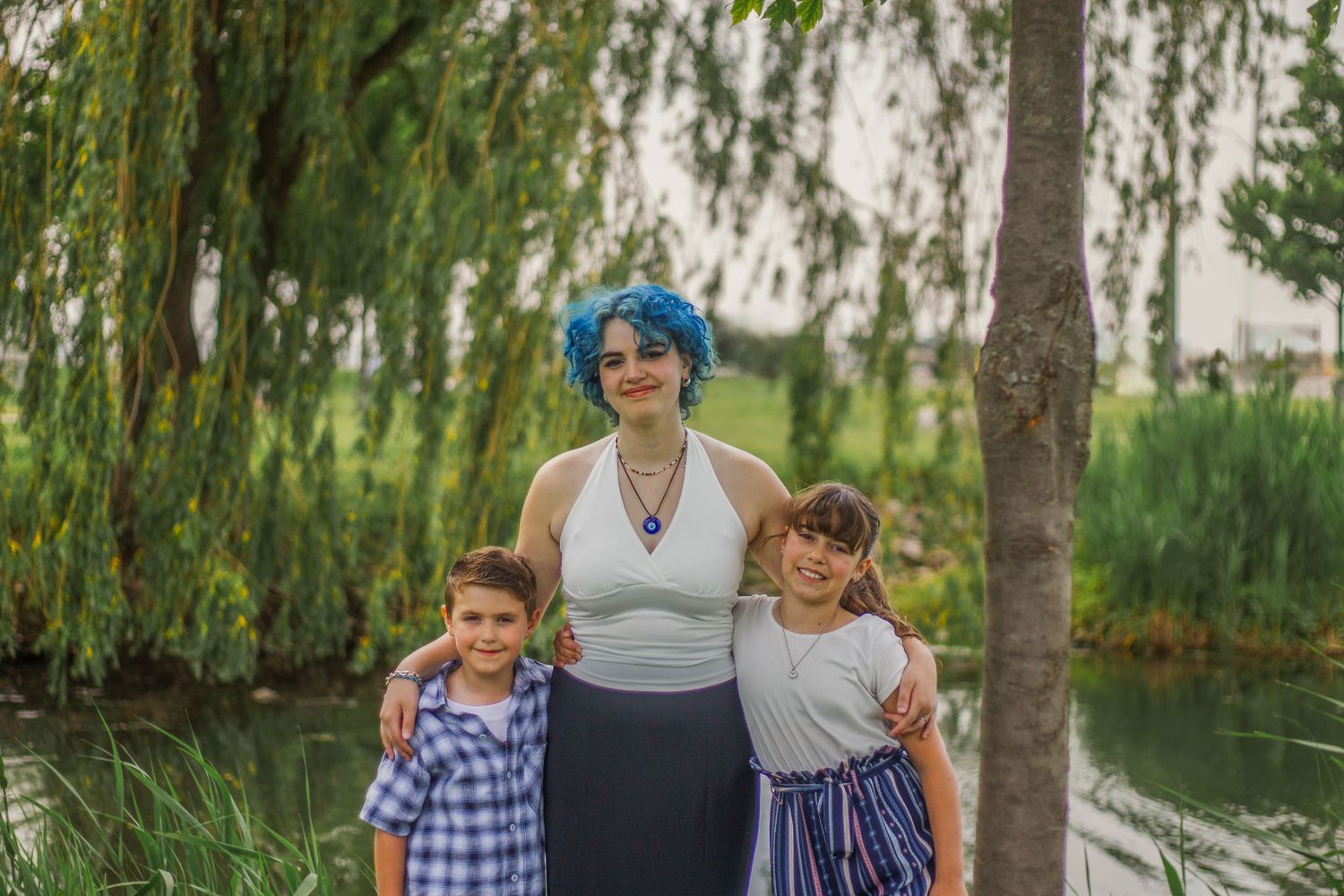 Family gathering under weeping willow trees near a peaceful lake.