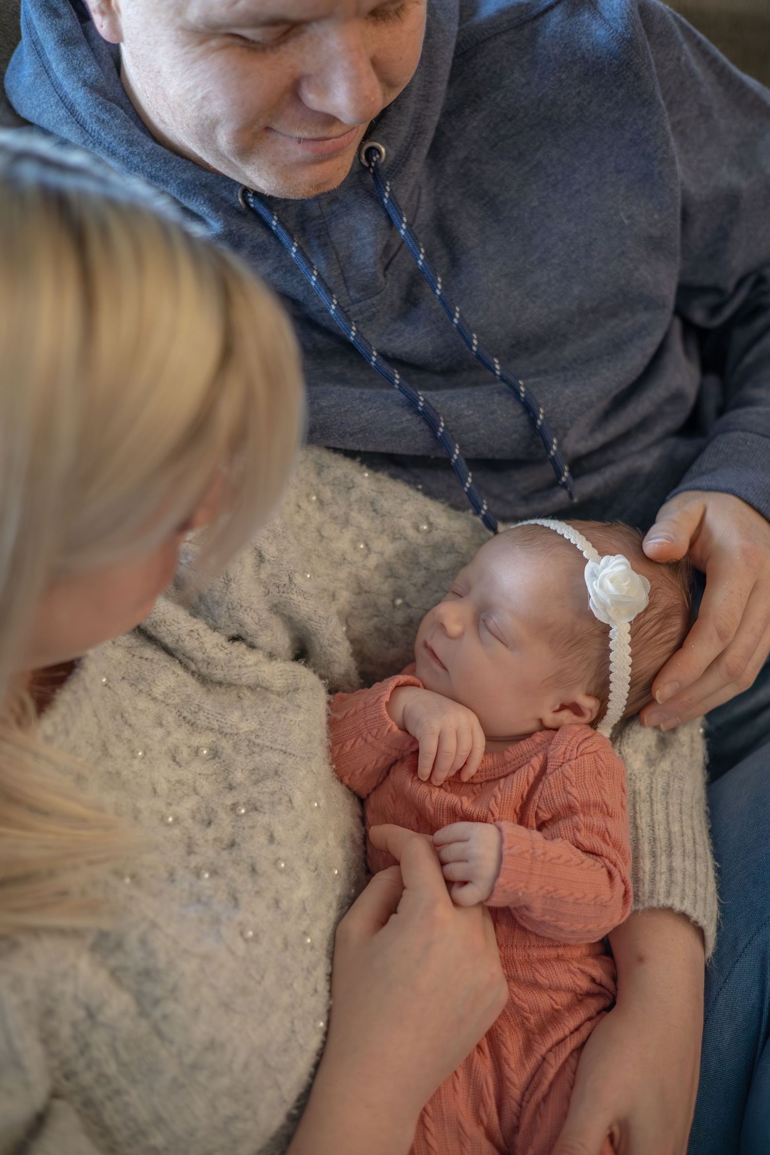 A sequence of tender moments showing hands gently caring for an infant wearing a coral-colored outfit.