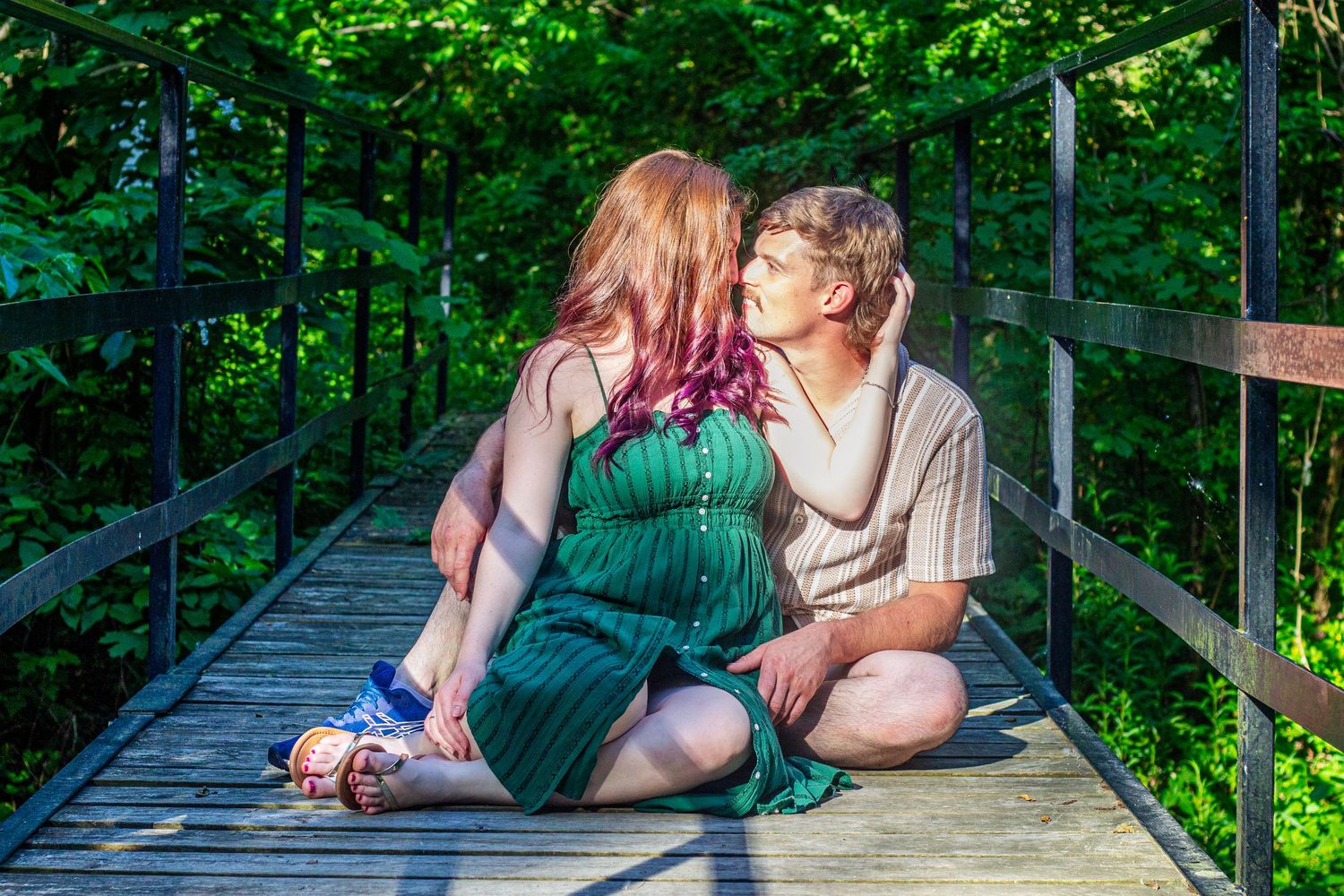 Couple sitting close together on wooden bridge surrounded by green forest.