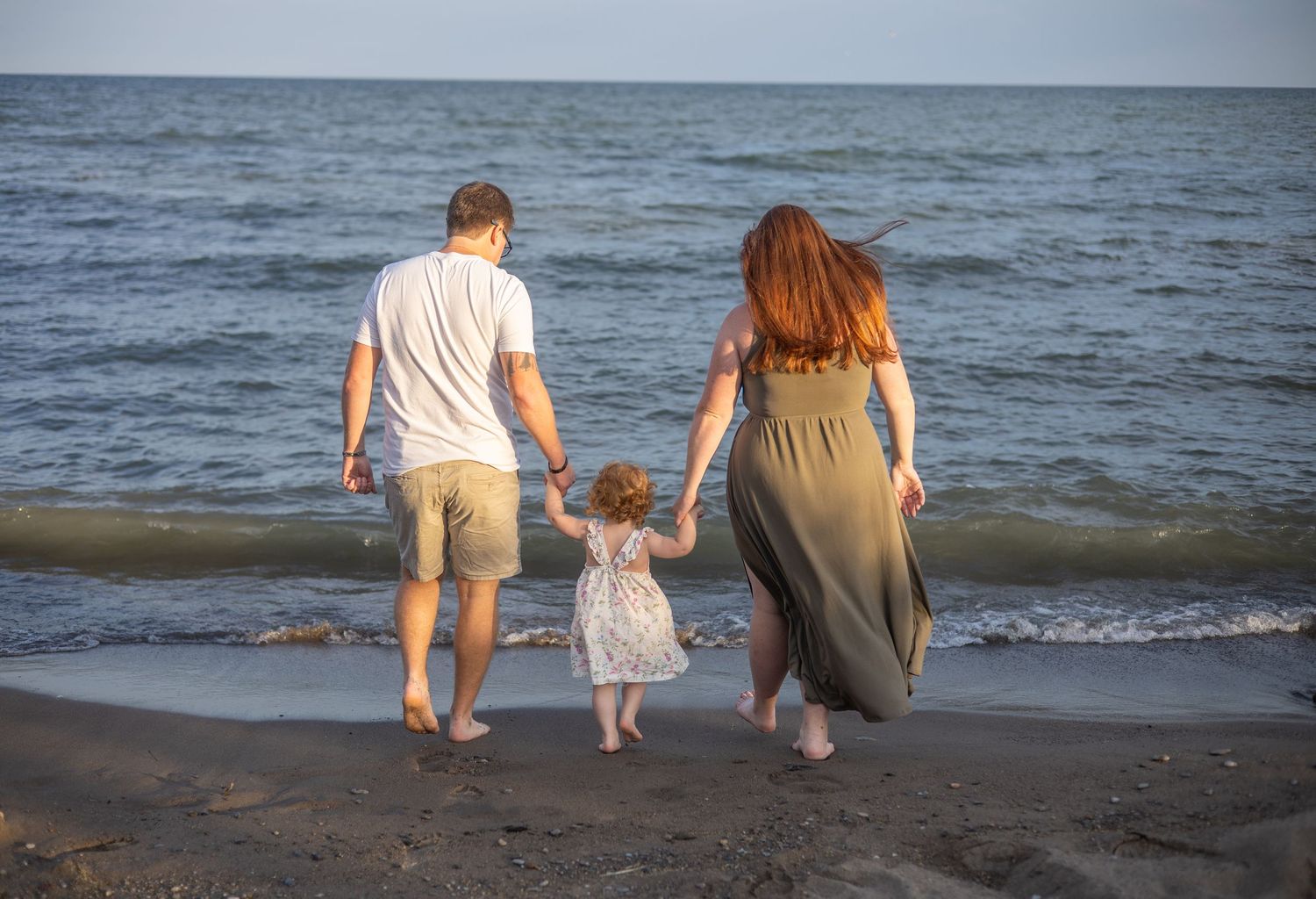 Family walking along the beach at sunset with waves crashing on the shore.