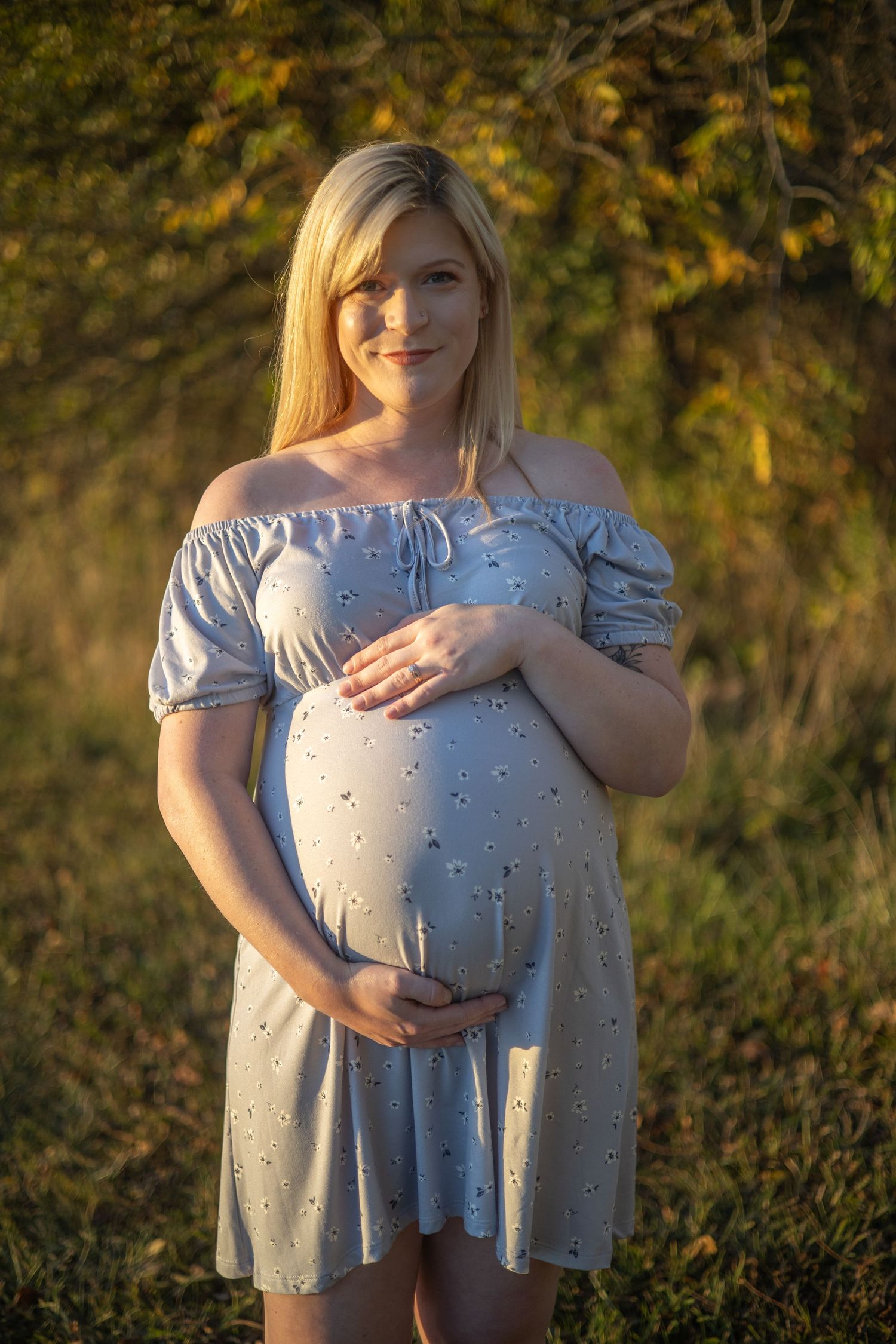 A pregnant woman in an off-shoulder dress poses in warm evening light.