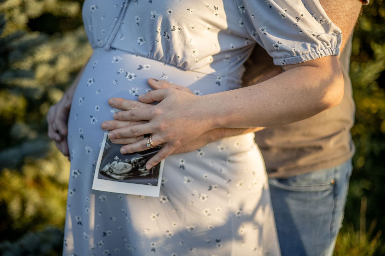 Hands holding an ultrasound photo against a pregnant belly in soft lighting. During maternity session