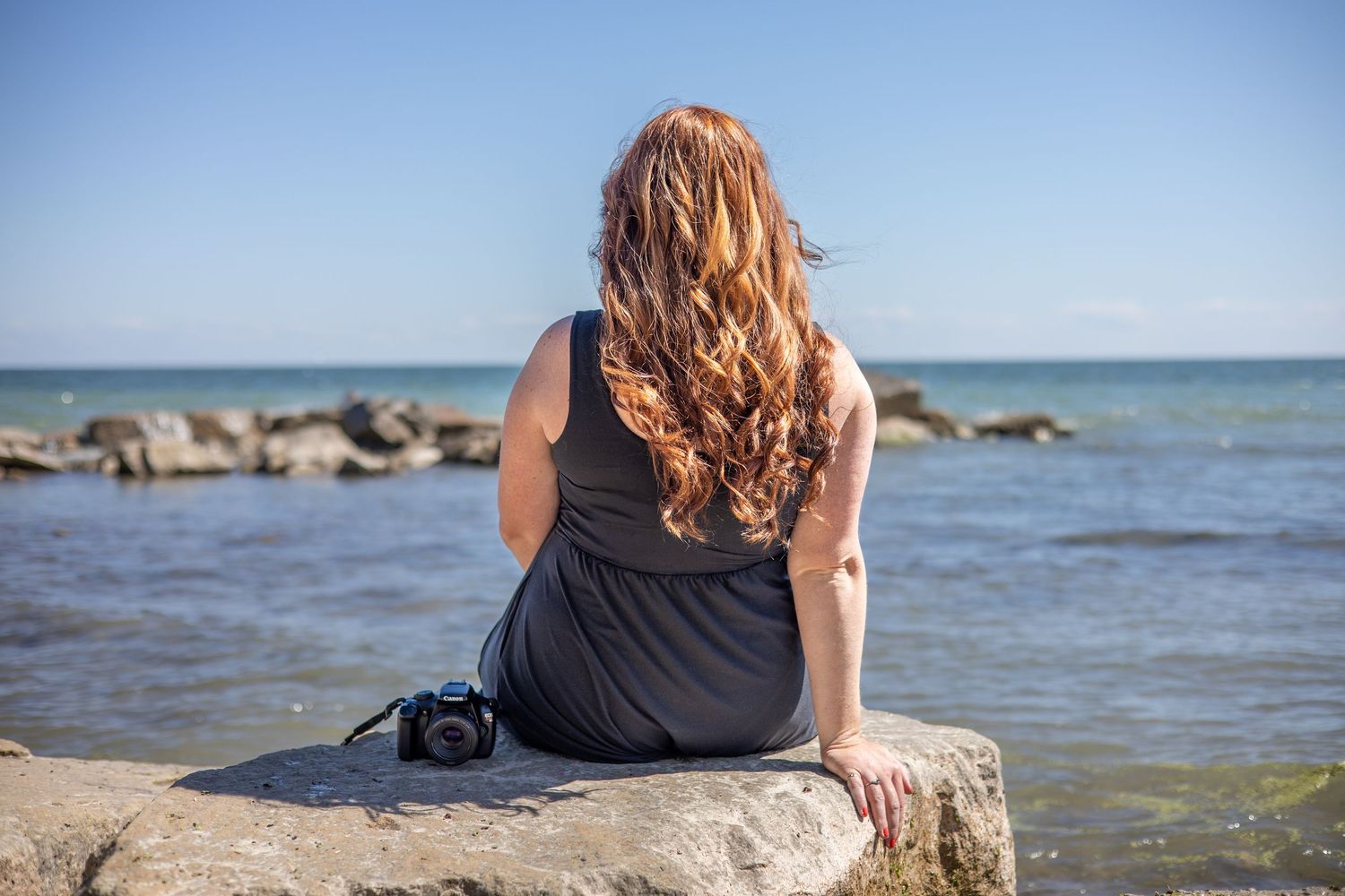 Person sitting on rocky shoreline looking out at calm lake waters.