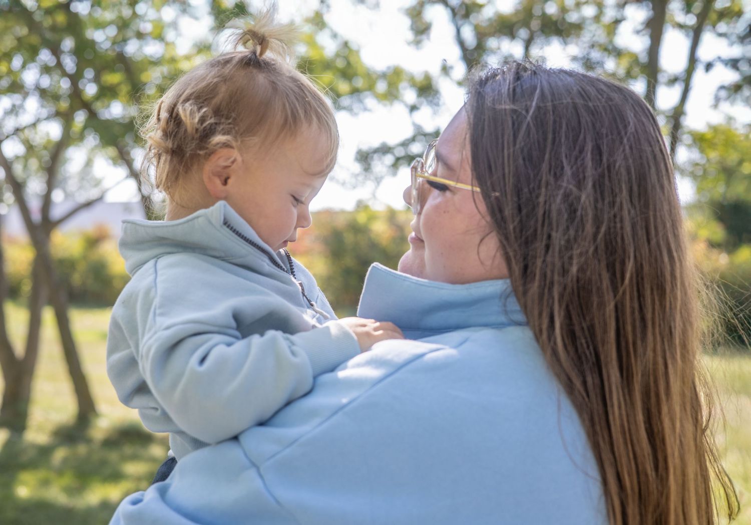 People in matching blue hoodies embrace in a sunny outdoor setting.