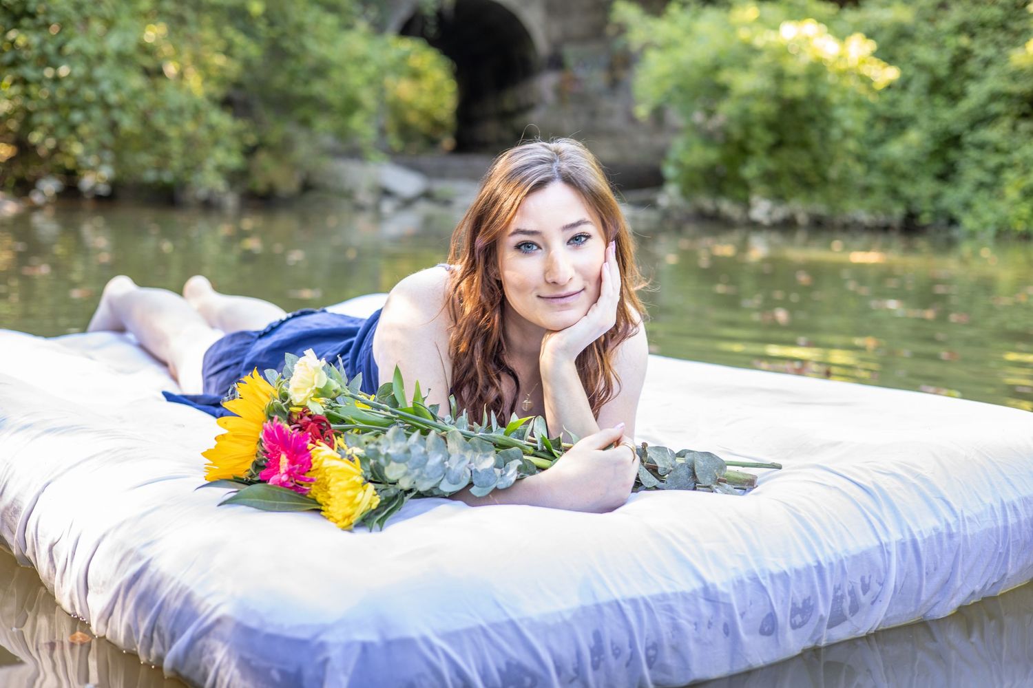 A dreamy portrait on a mattress with colorful flowers by on a pond. During Portrait session