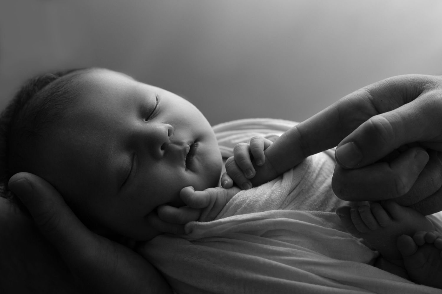 Black and white sequence of photos showing hands gently holding and caring for a newborn baby.