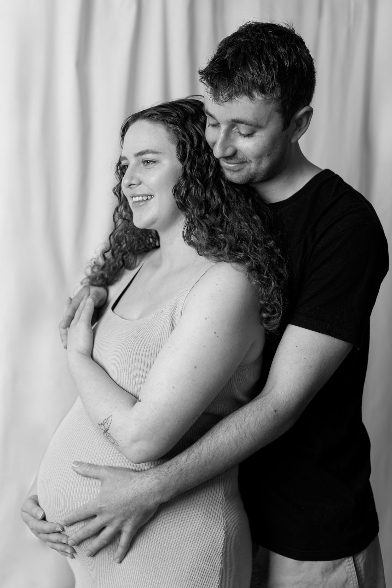 A series of four black and white maternity photos showing a couple embracing with the woman wearing a white tank top.