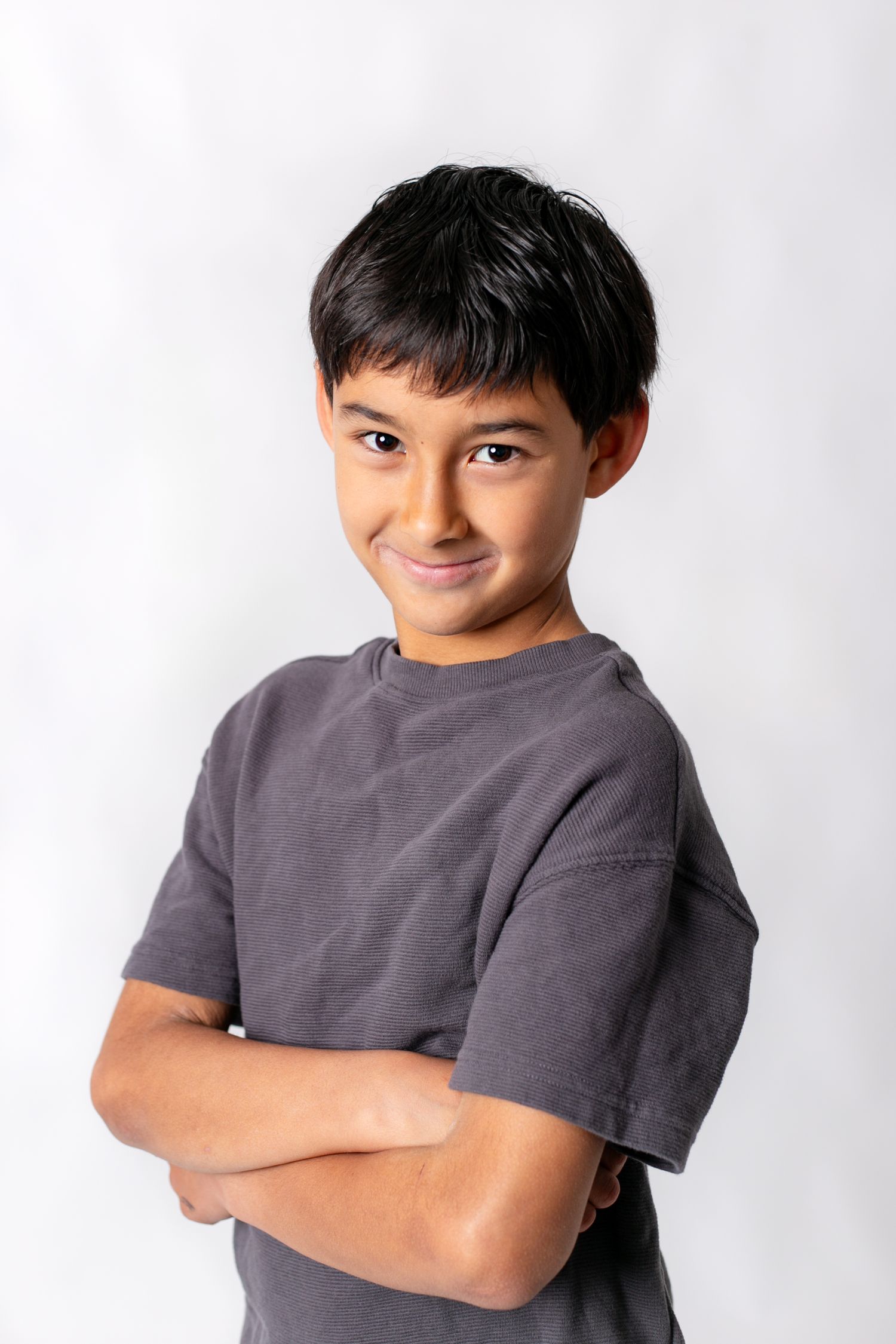 Young person in grey t-shirt poses with crossed arms against white background.