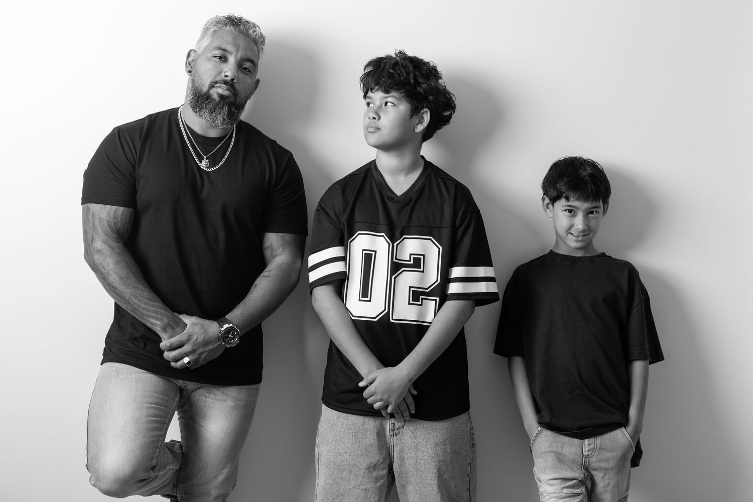 Three people in casual wear pose against white background for family portrait.