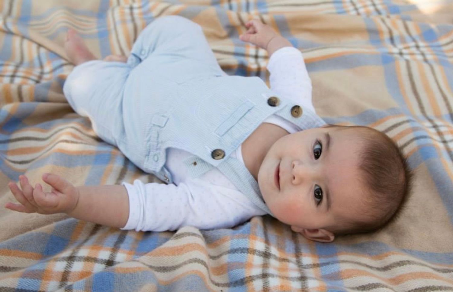 Infant in light blue outfit lying on plaid blanket showing developmental milestones.