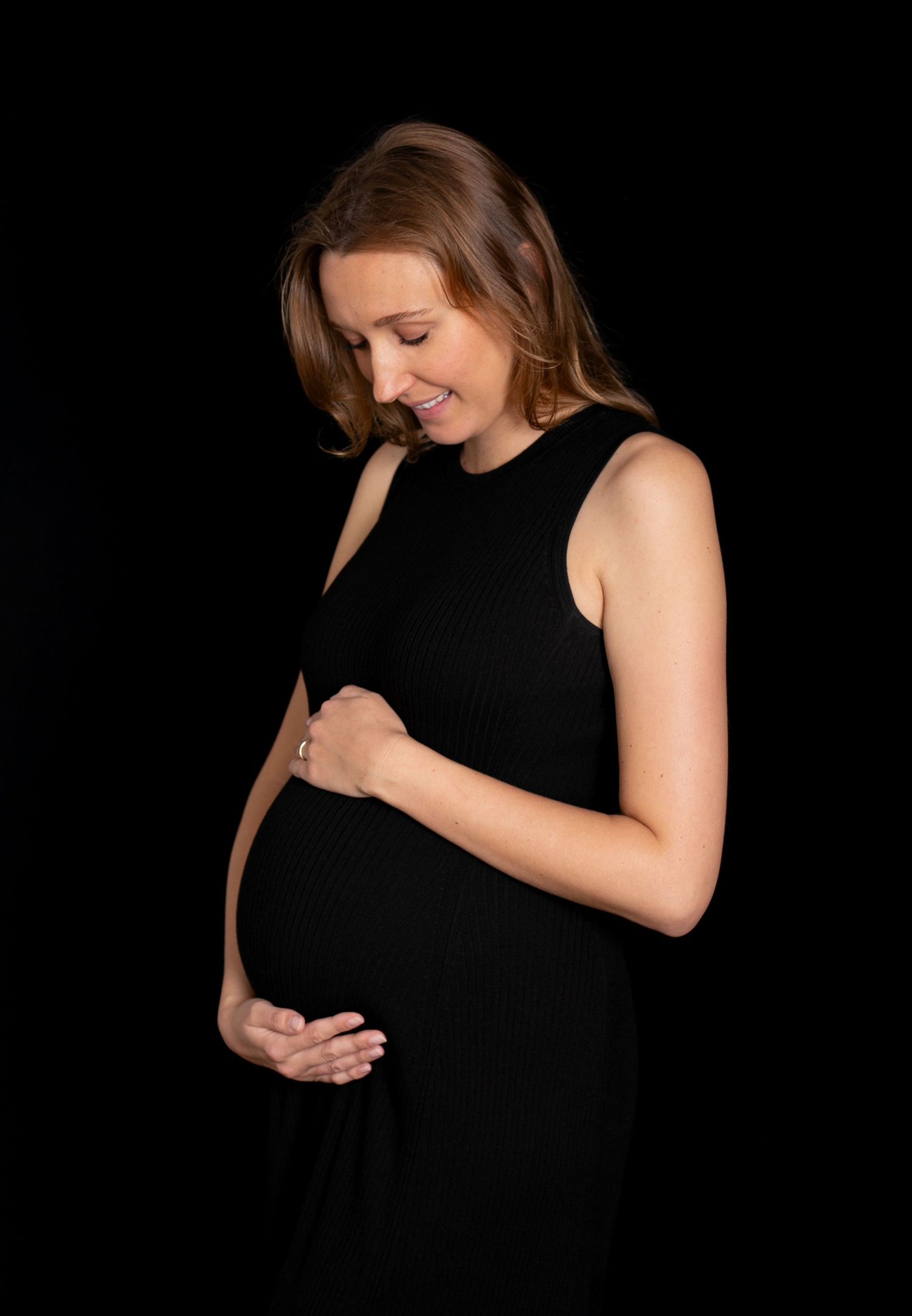 A series of black and white maternity photos showing a pregnant woman in a black dress against a dark background.