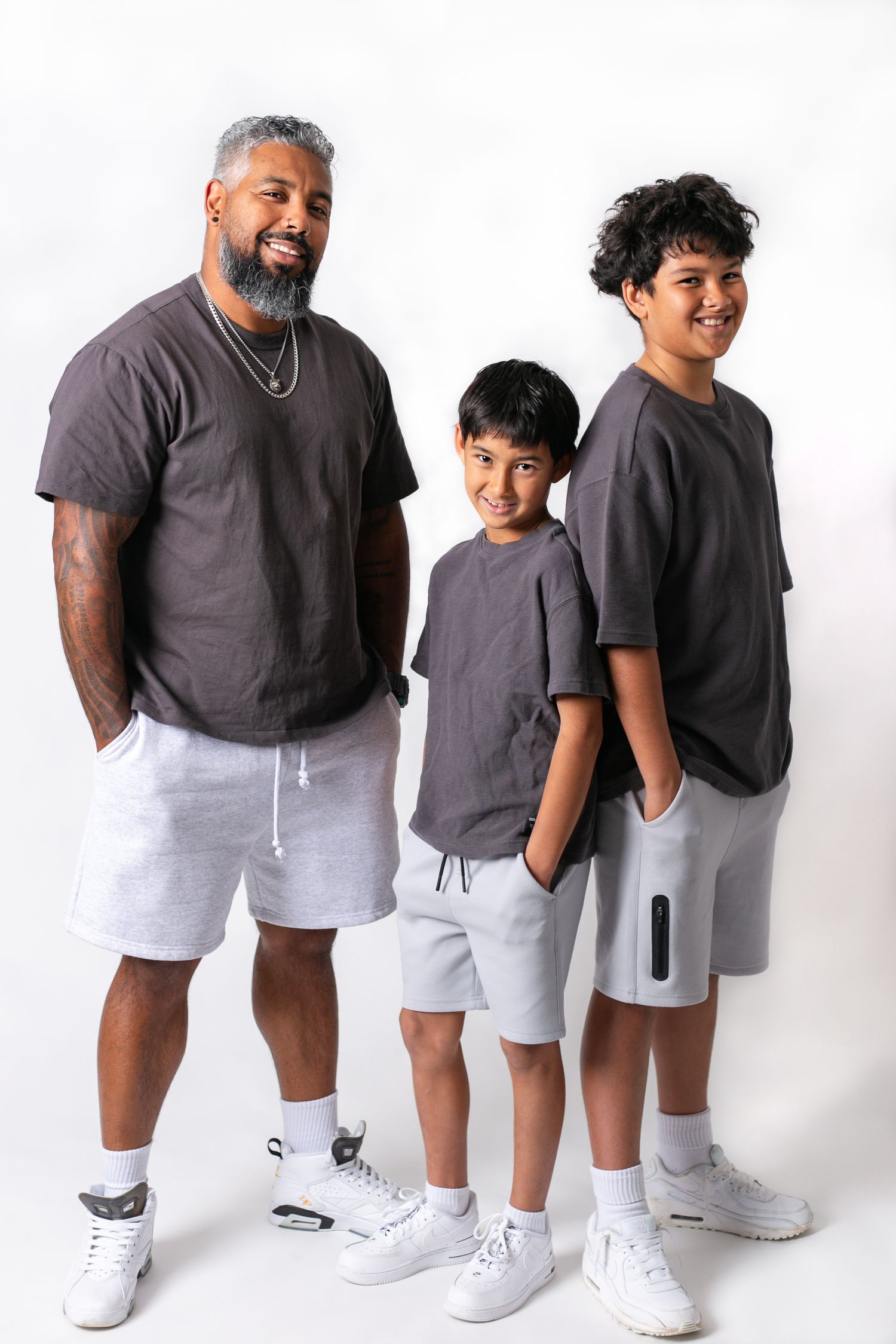 Family members pose together in coordinated gray and white casual outfits against white backdrop.