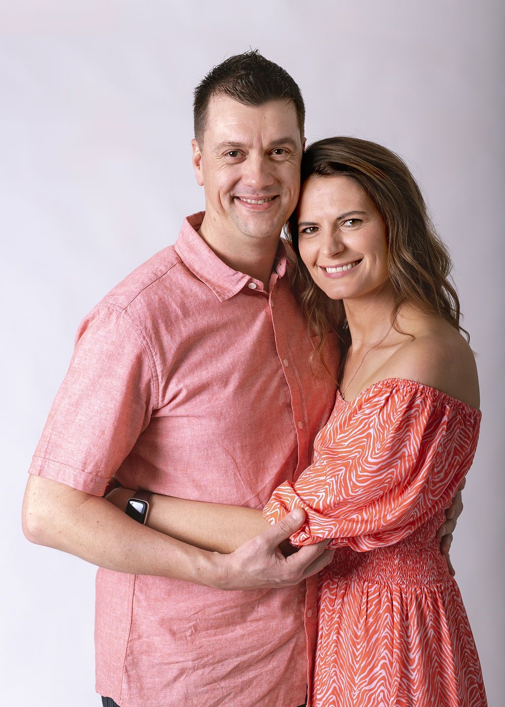 Couple in coordinating coral outfits posing together against white studio background at Gabriella Aranky Photography studio, Auckland.