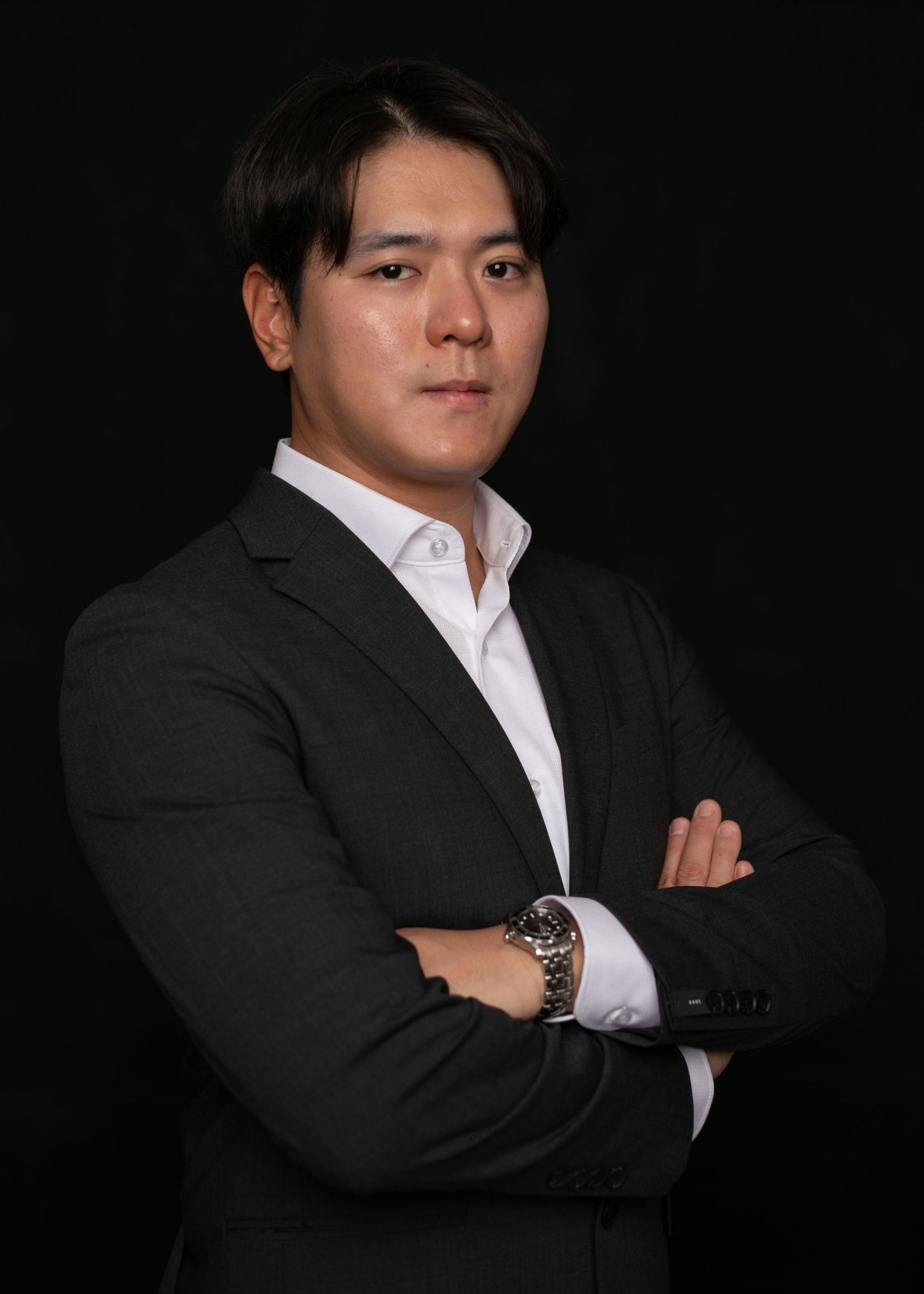 Professional Asian businessman in dark suit with arms crossed against black background, confident corporate portrait.