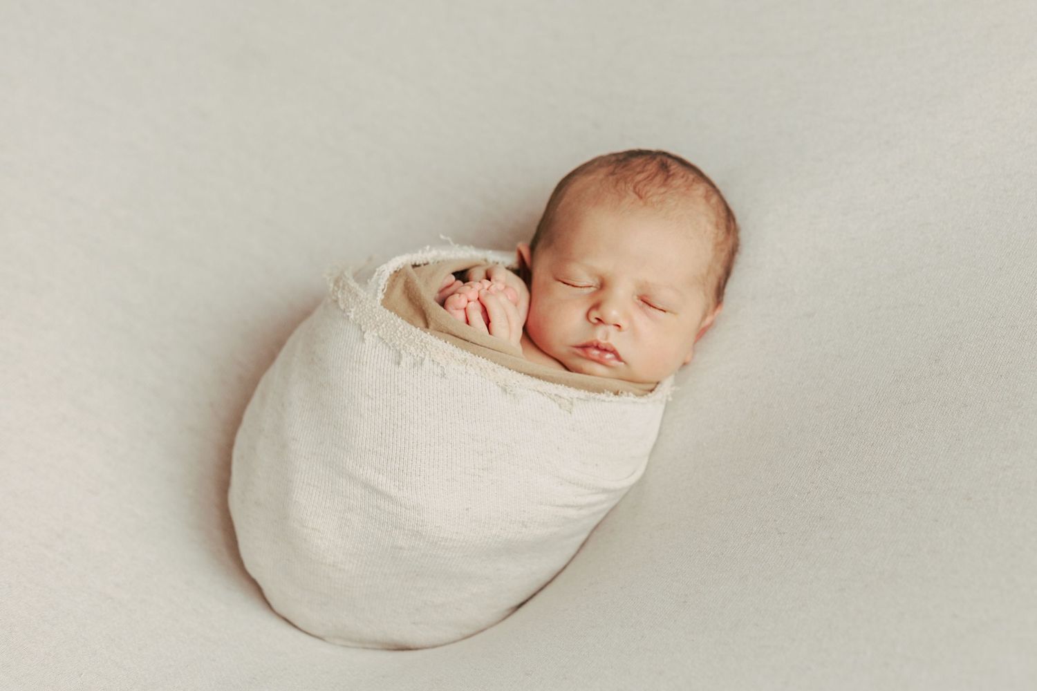 Minimalist newborn photography series with baby wrapped in white against light background.