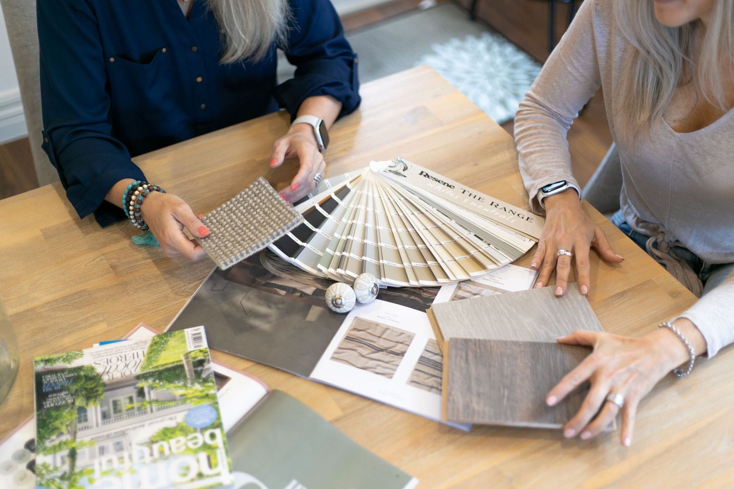 Two people reviewing paint swatches and material samples on a wooden table during an interior design consultation.