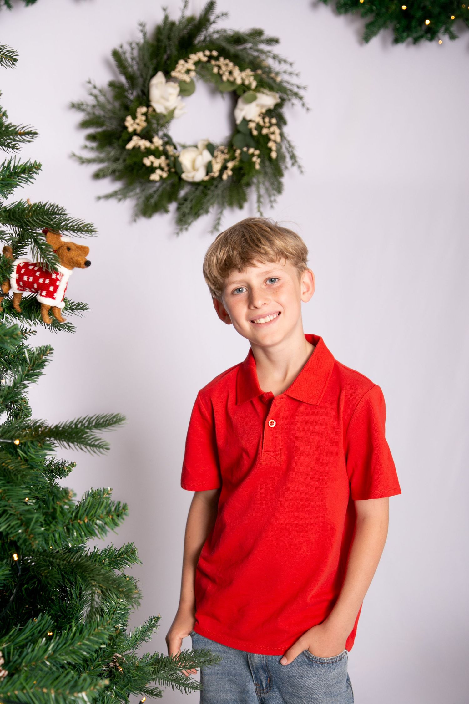 Holiday portrait series showing a child in a red polo shirt posing next to a decorated Christmas tree.