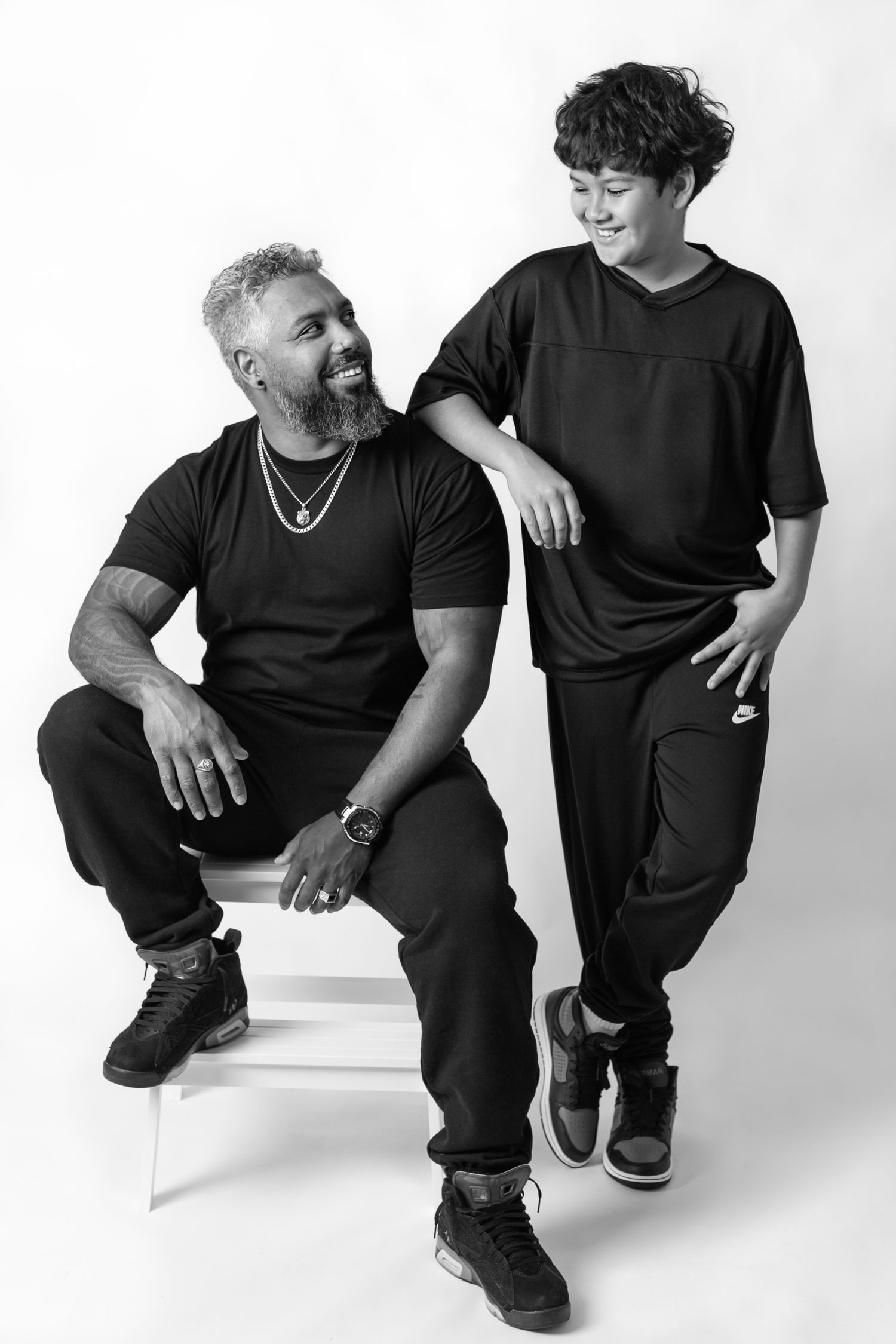 Black and white portrait of two people in casual wear posing against white background.