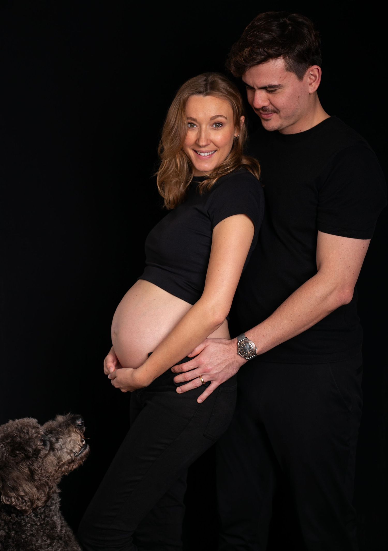 A maternity photo series showing a couple in black against dark background as pregnancy progresses through multiple stages.