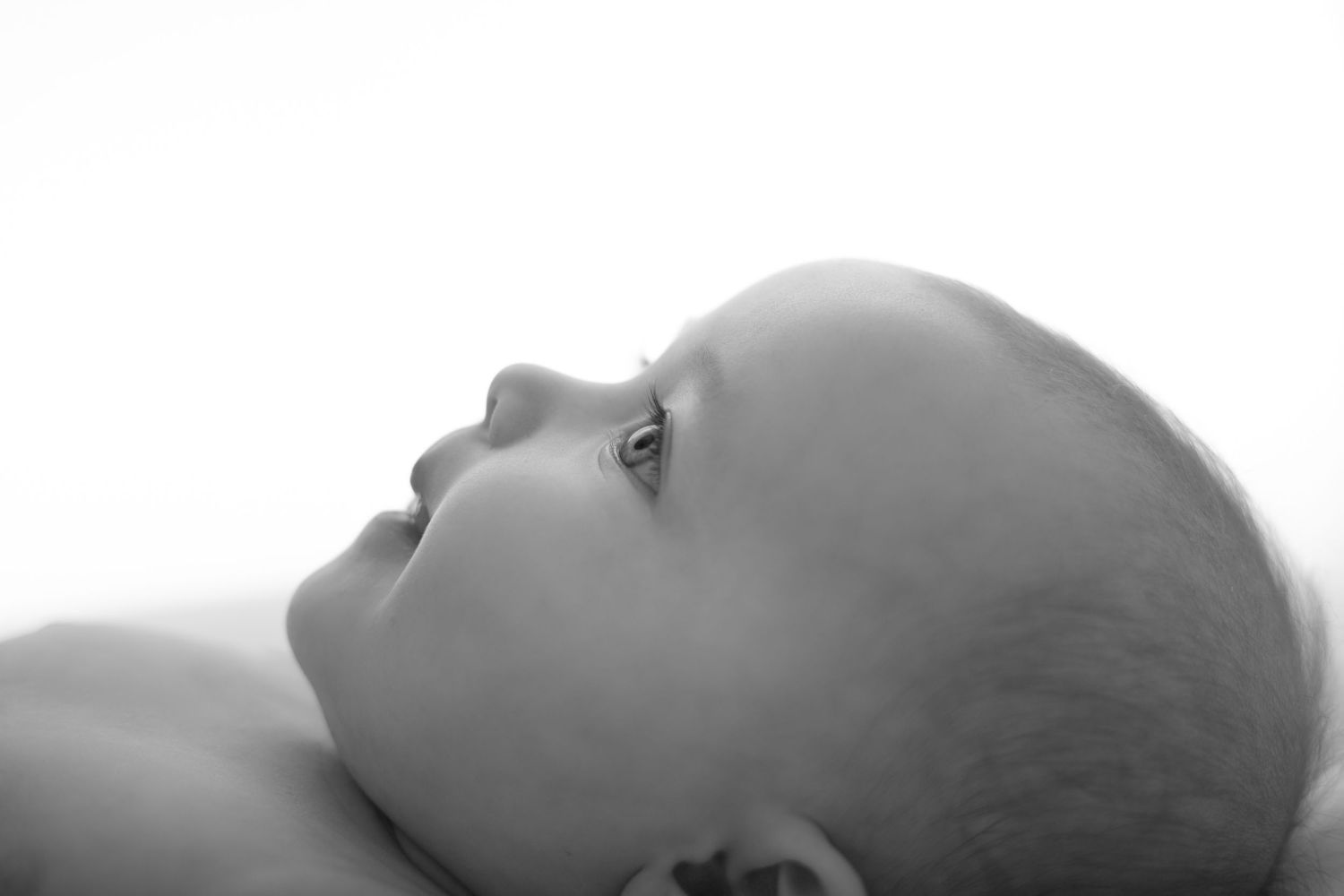 Black and white close-up portrait of a peaceful newborn baby lying down, looking upward.