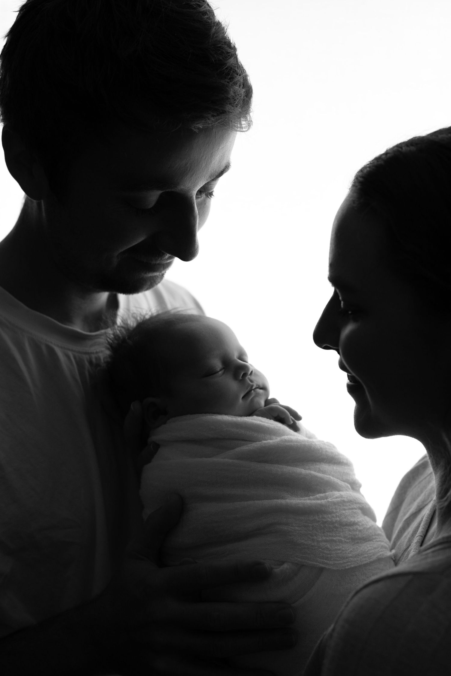 A series of black and white silhouettes showing intimate moments between parent and baby in dramatic lighting.