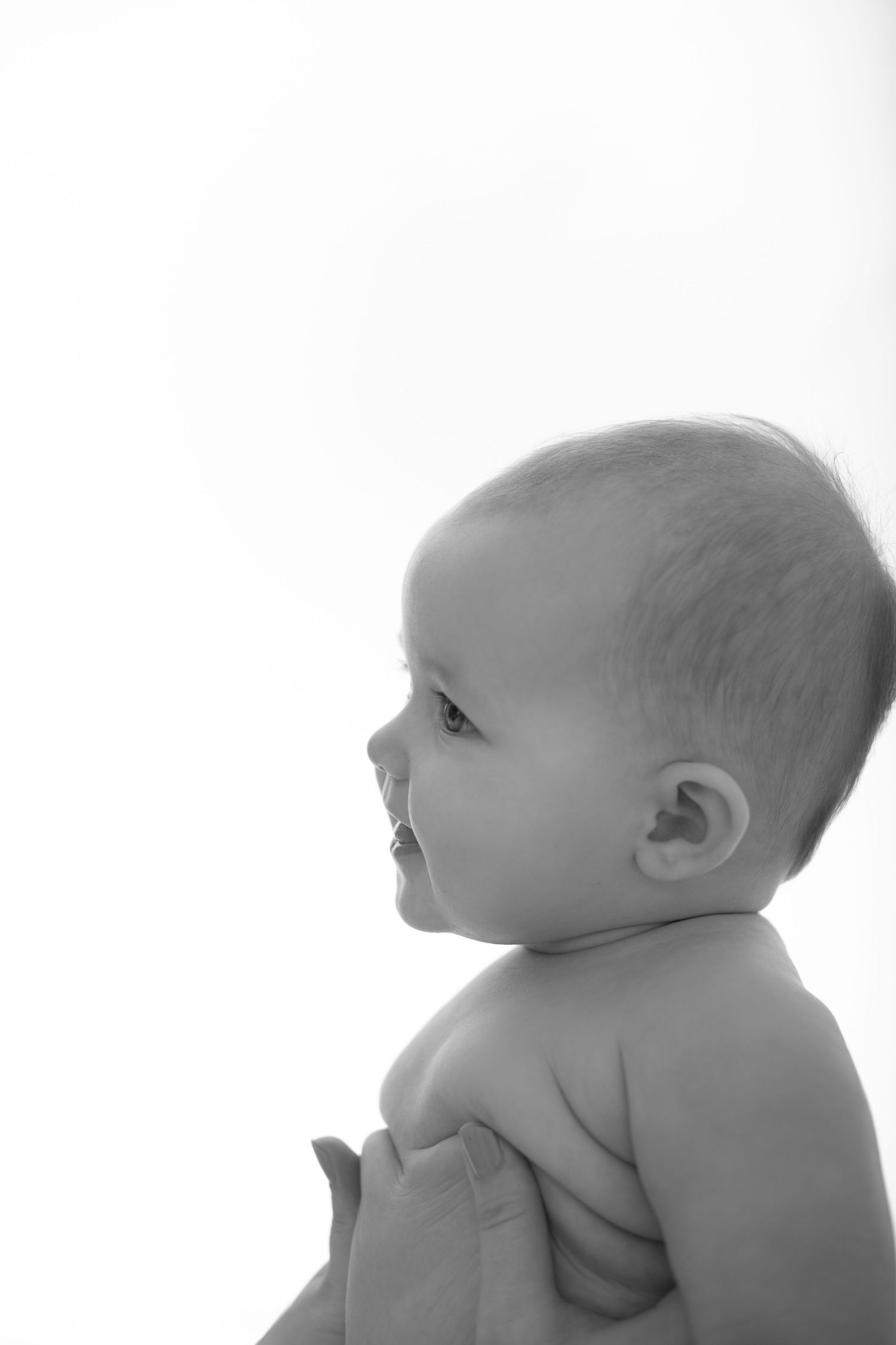 Black and white portrait of a cute baby looking sideways, captured in soft light against a white background.