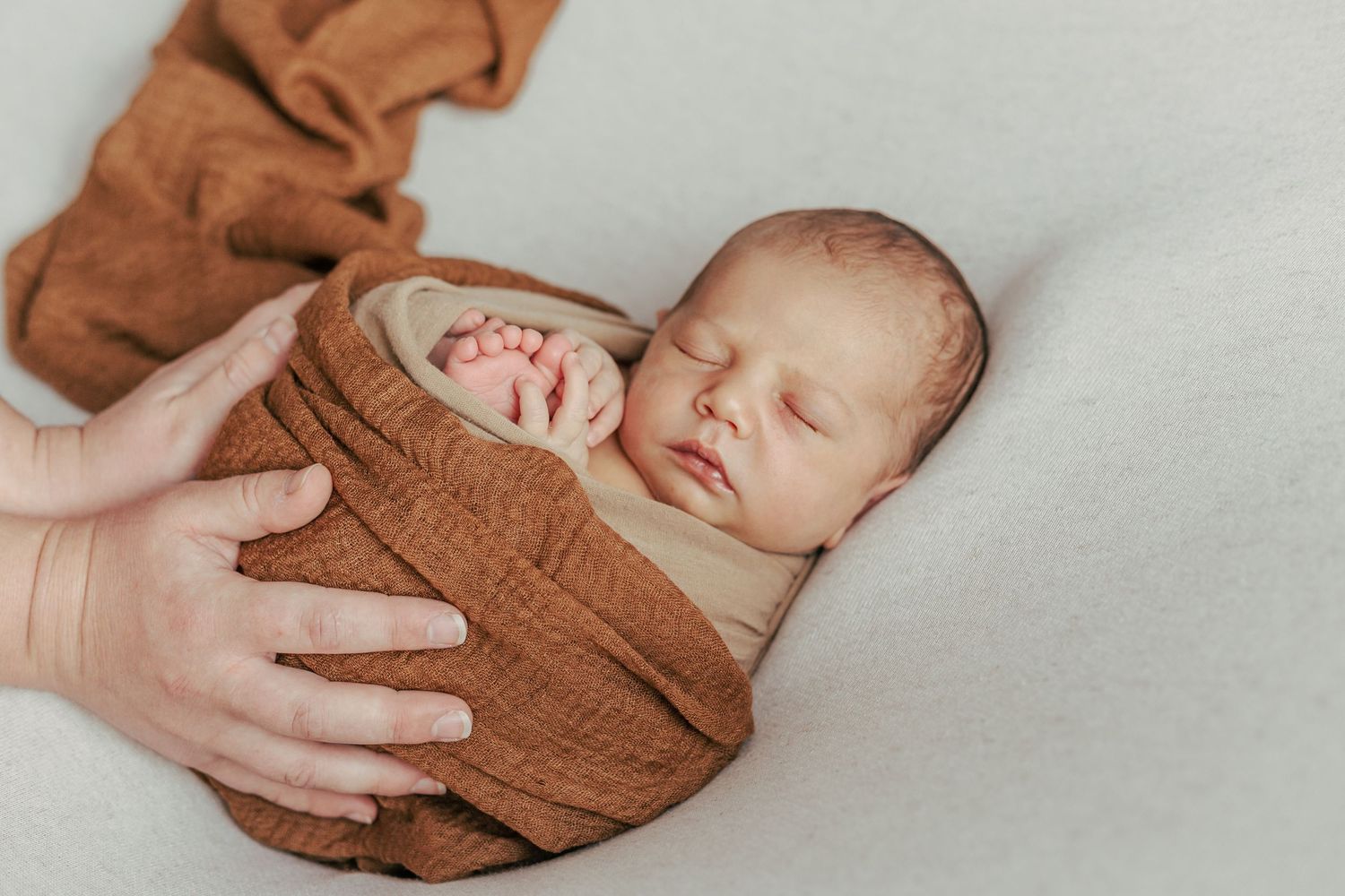 Newborn baby wrapped in brown fabric against neutral background in sequential poses.