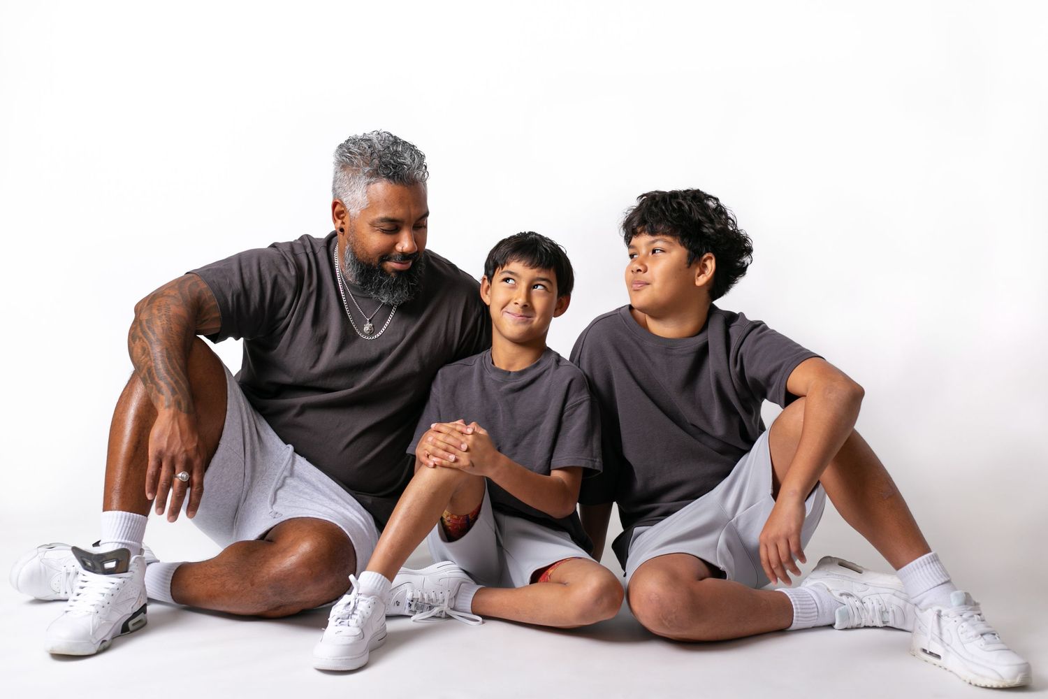 Family wearing matching grey outfits sitting together on white background.