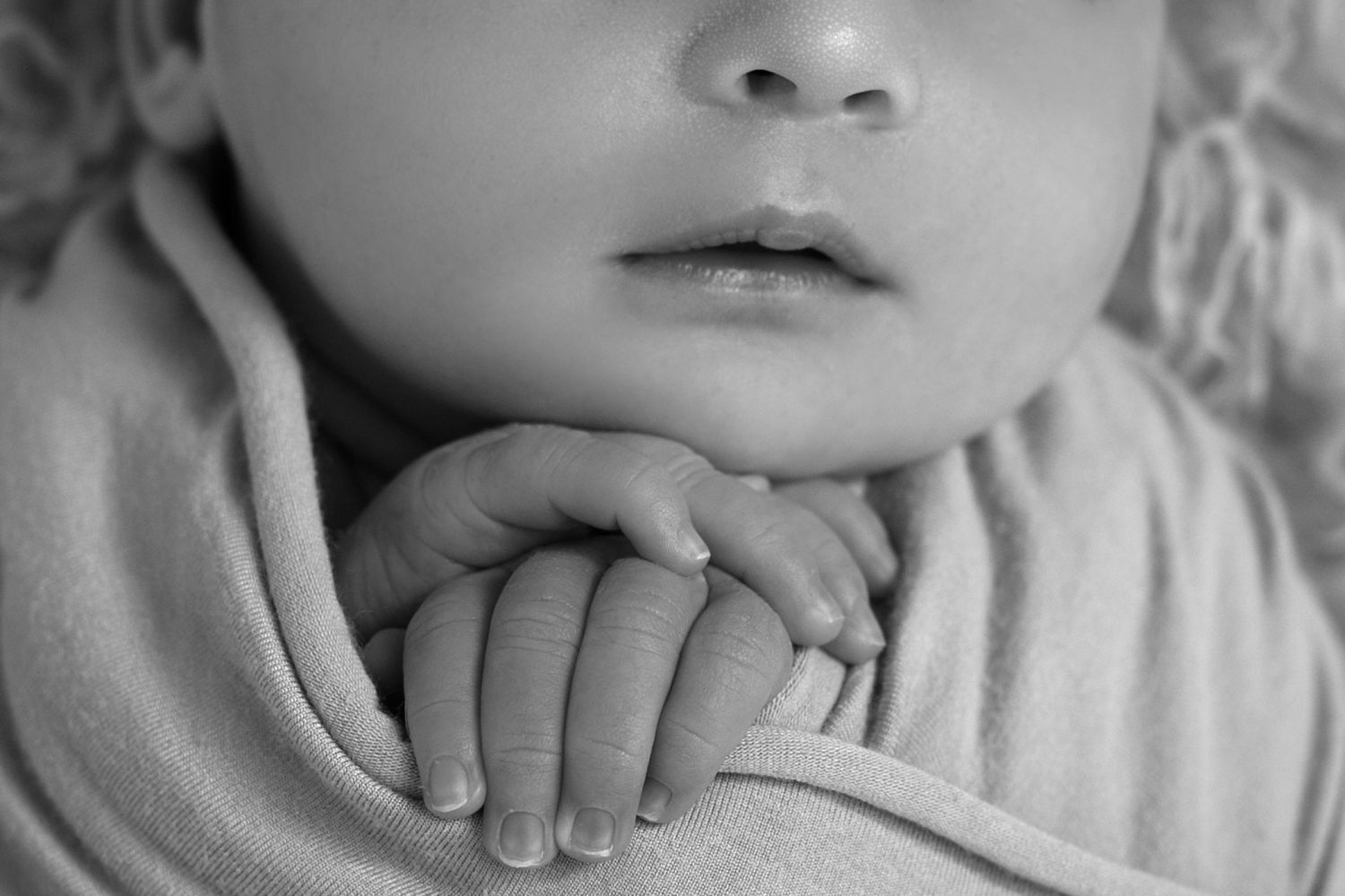 Close-up black and white photograph showing tiny newborn baby fingers grasping gently.