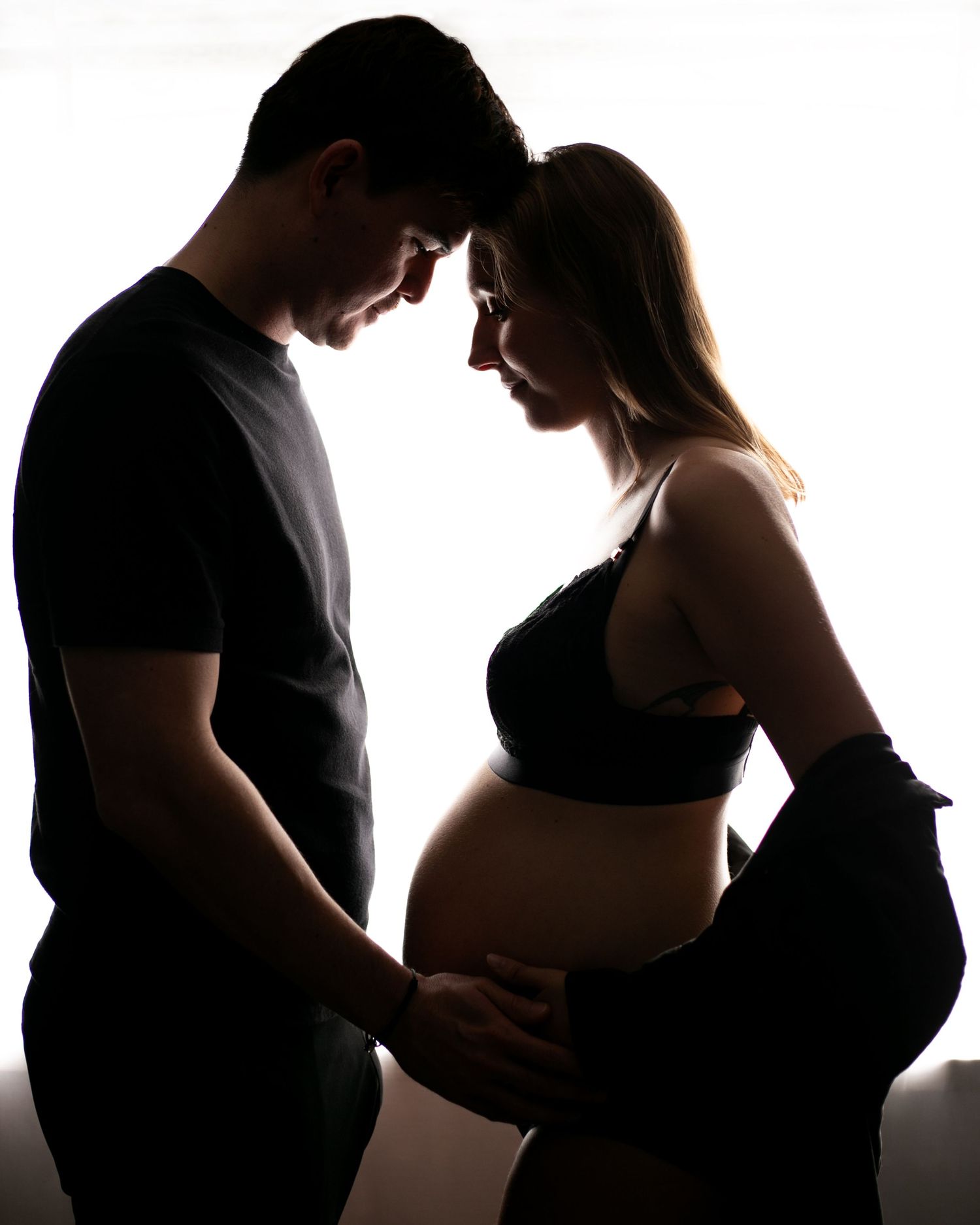 A silhouetted series of couples in intimate poses against a bright white backdrop creates a romantic maternity montage.